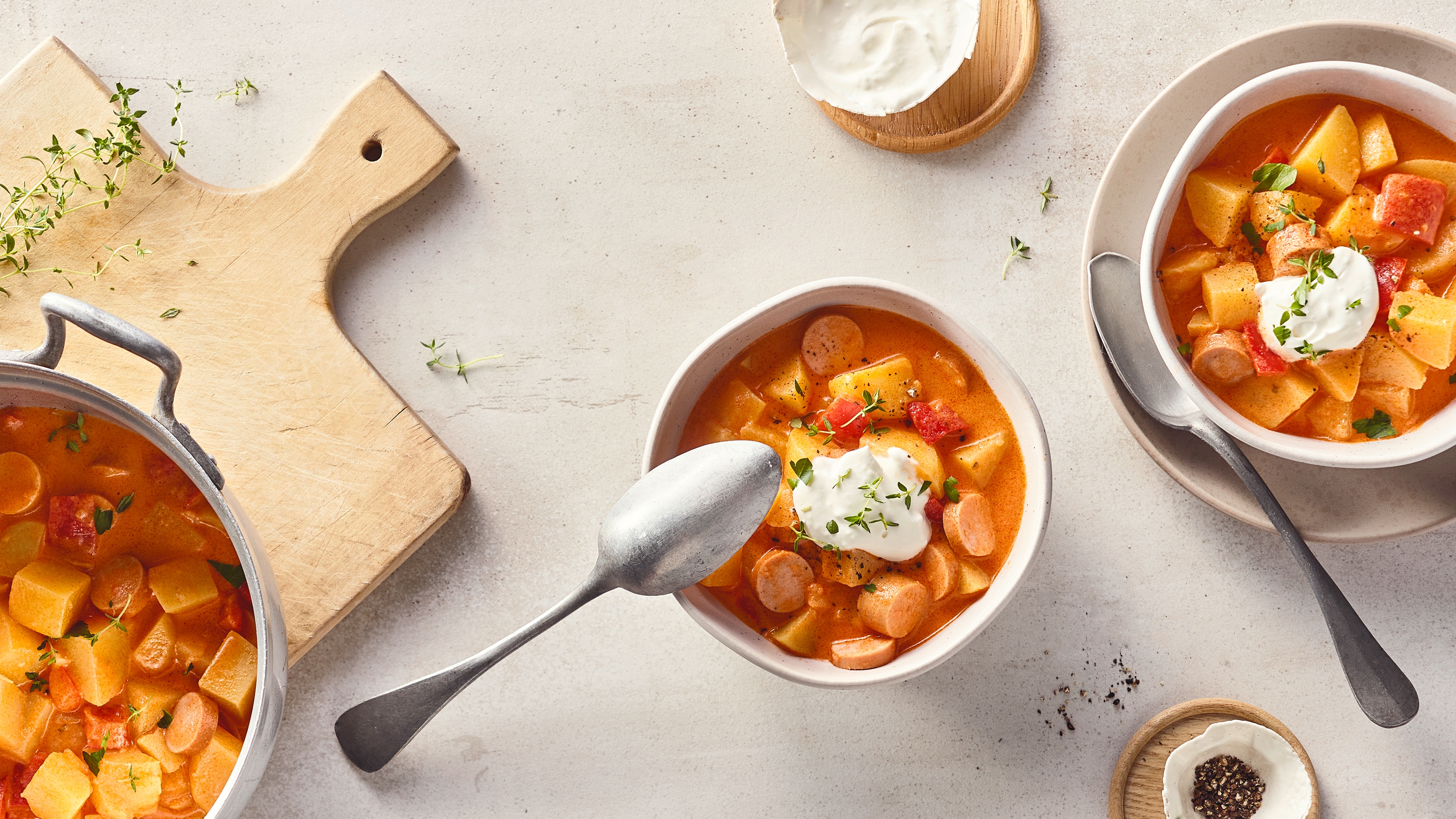 Rezept für Kartoffelgulasch mit Würstchen Schalen, befüllt mit einer hellen Suppe aus Kartoffeln, Paprika und Würstchen, getoppt mit weißer Creme und frischen Kräutern