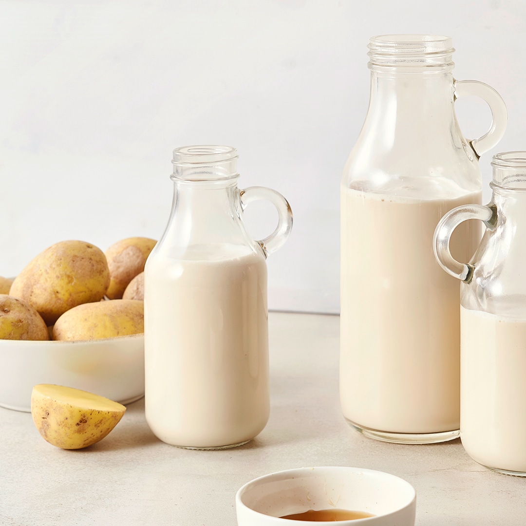 Drei Glasflaschen mit weißer Flüssigkeit, daneben eine Schale mit Kartoffeln und ein halbierter Kartoffel.