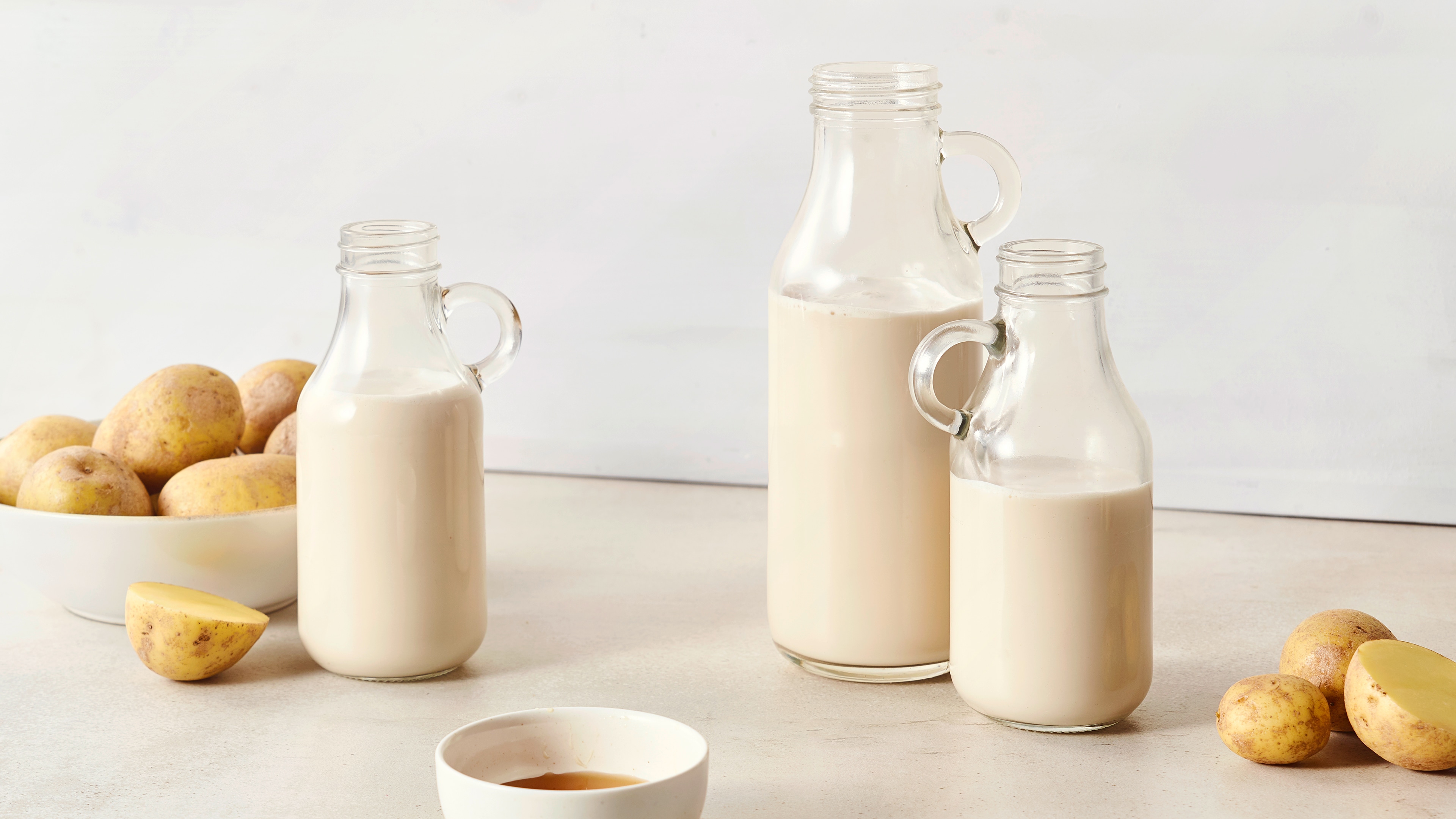 Drei Glasflaschen mit weißer Flüssigkeit, daneben eine Schale mit Kartoffeln und ein halbierter Kartoffel.