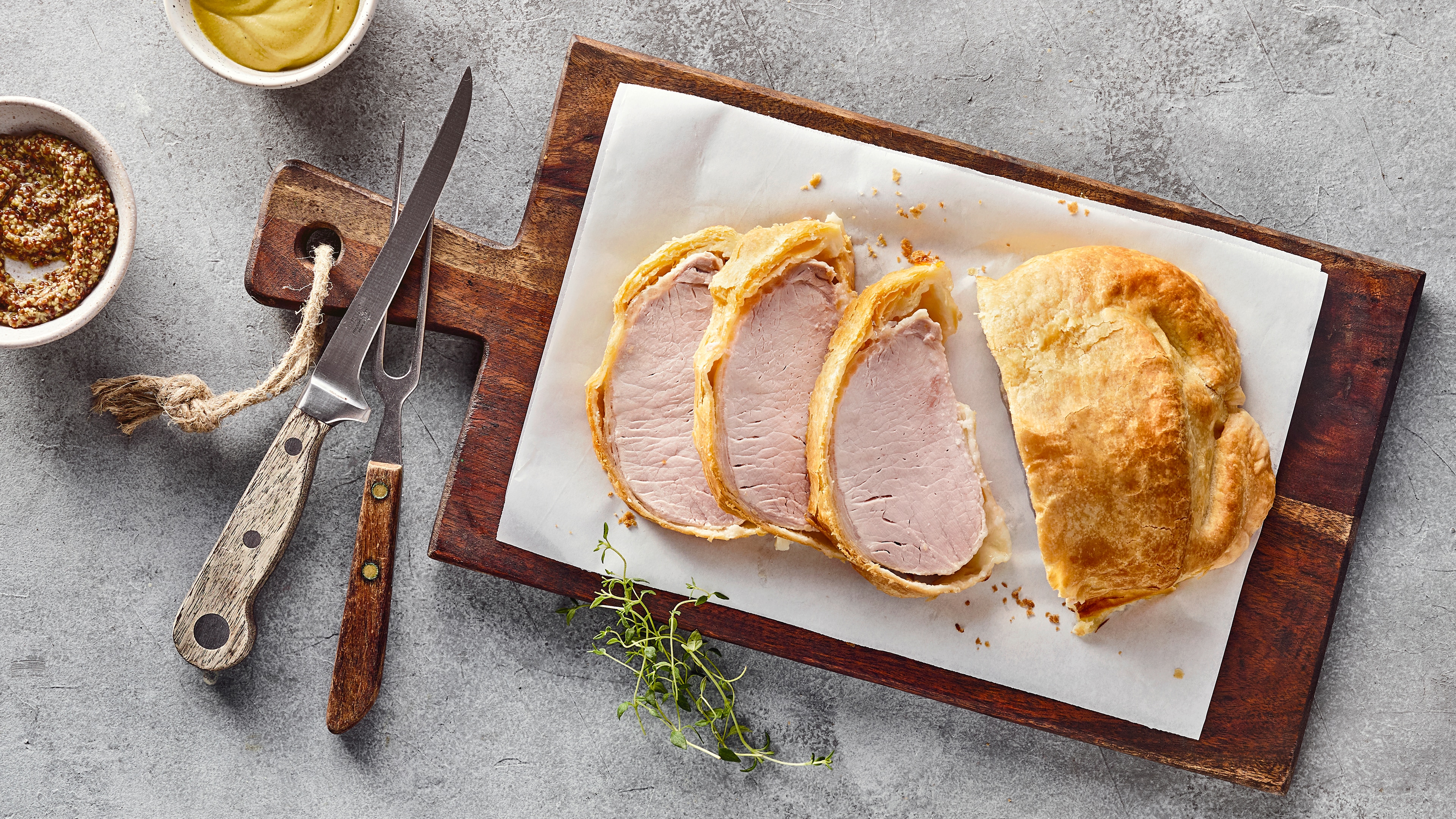Rezept für Kassler im Blätterteig Ein großes Stück zartrosa Fleisch, ummantelt mit gelbgold gebackenem Blätterteig, auf einem rustikalen Holzbrett