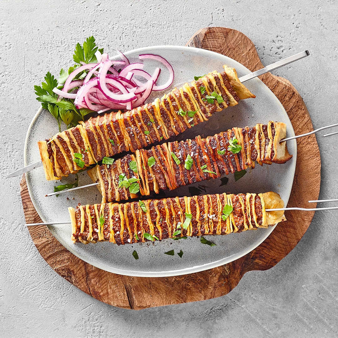 Drei Schaschlikspieße mit abwechselnd aufgespießtem Wrap und Hackfleisch.