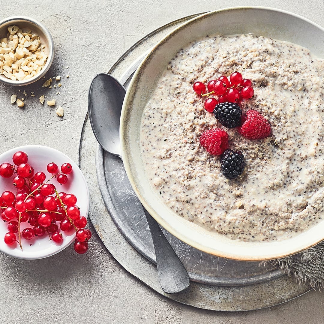 Eine helle Schüssel gefüllt mit einem cremigen Brei mit Chiasamen getoppt mit verschiedenen Beeren auf silbernen Teller