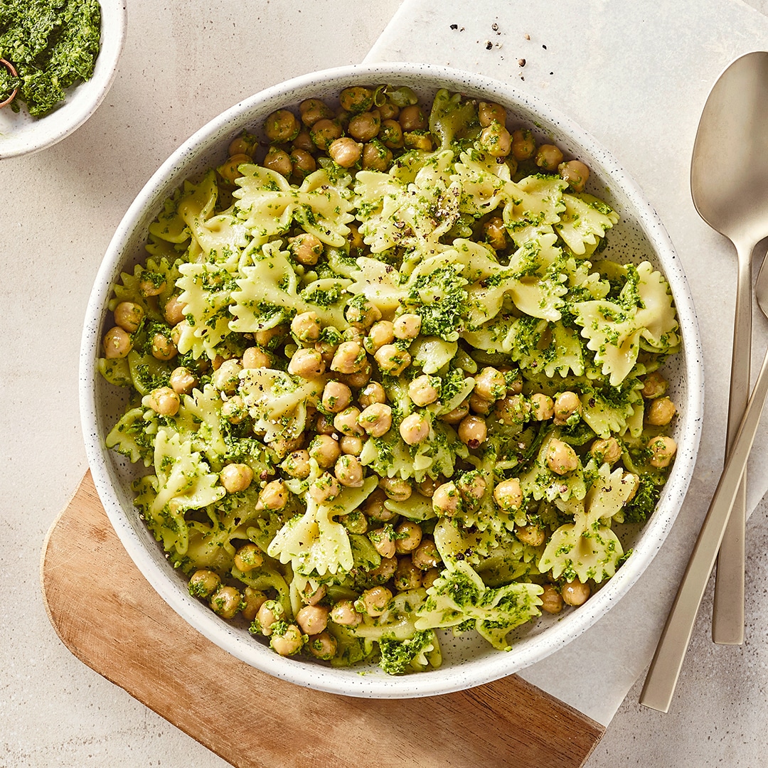 Eine Schüssel mit grüner Farfalle-Nudeln, hellen Kichererbsen & grüner Kräutermischung, daneben eine Schale mit Pesto.