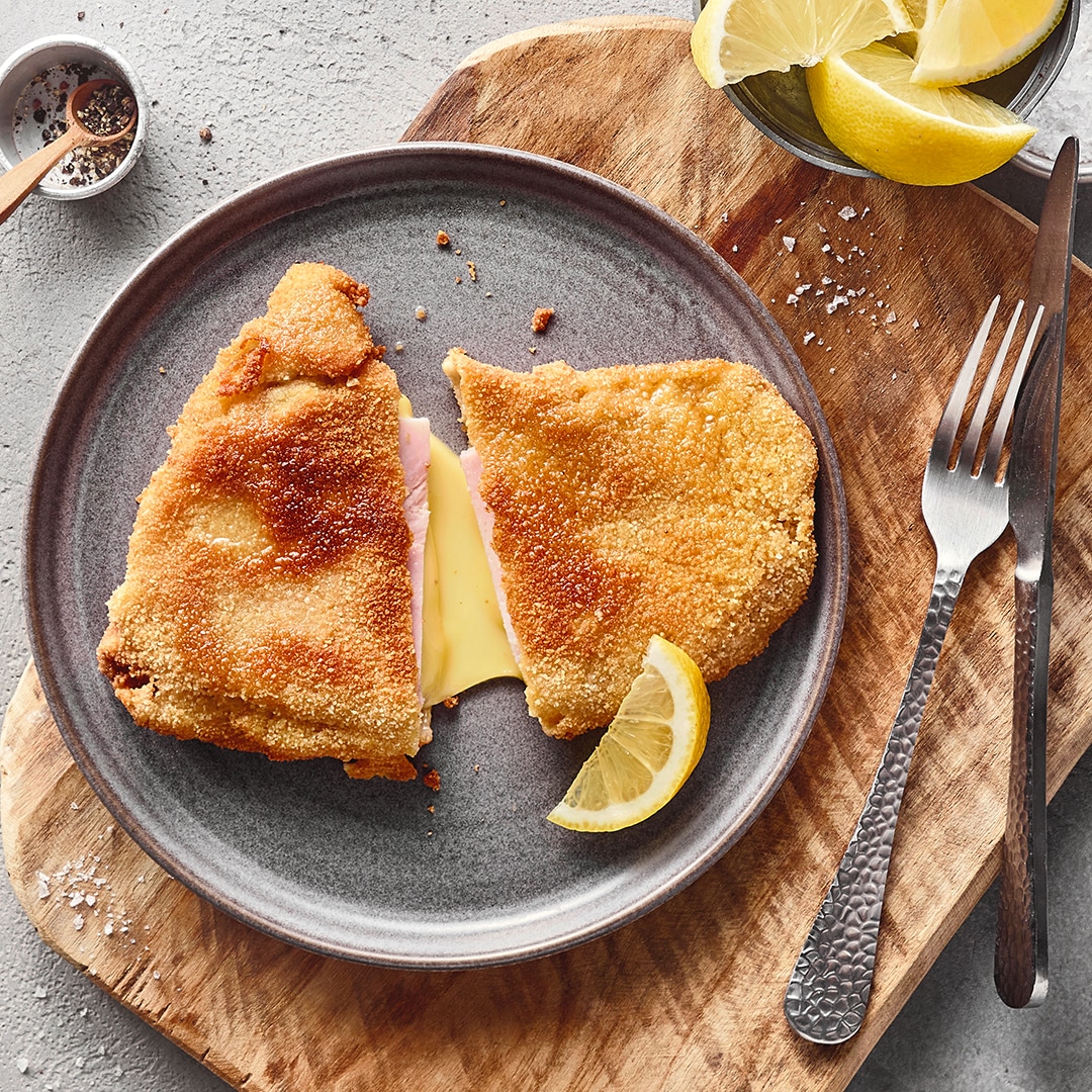 Ein Teller mit einem panierten Schnitzel, gefüllt mit Käse und Schinken, garniert mit einer Zitrone.