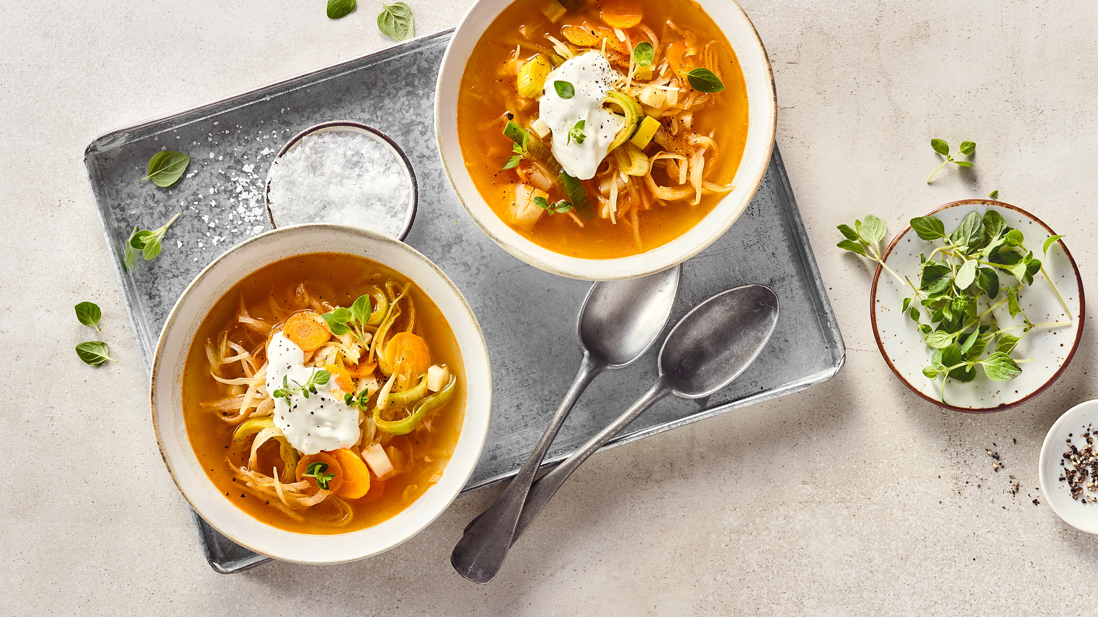 Eine Schüssel mit Karottenscheiben, Porree, Kohl in Gemüsebrühe, garniert mit frischen Kräutern und heller Creme