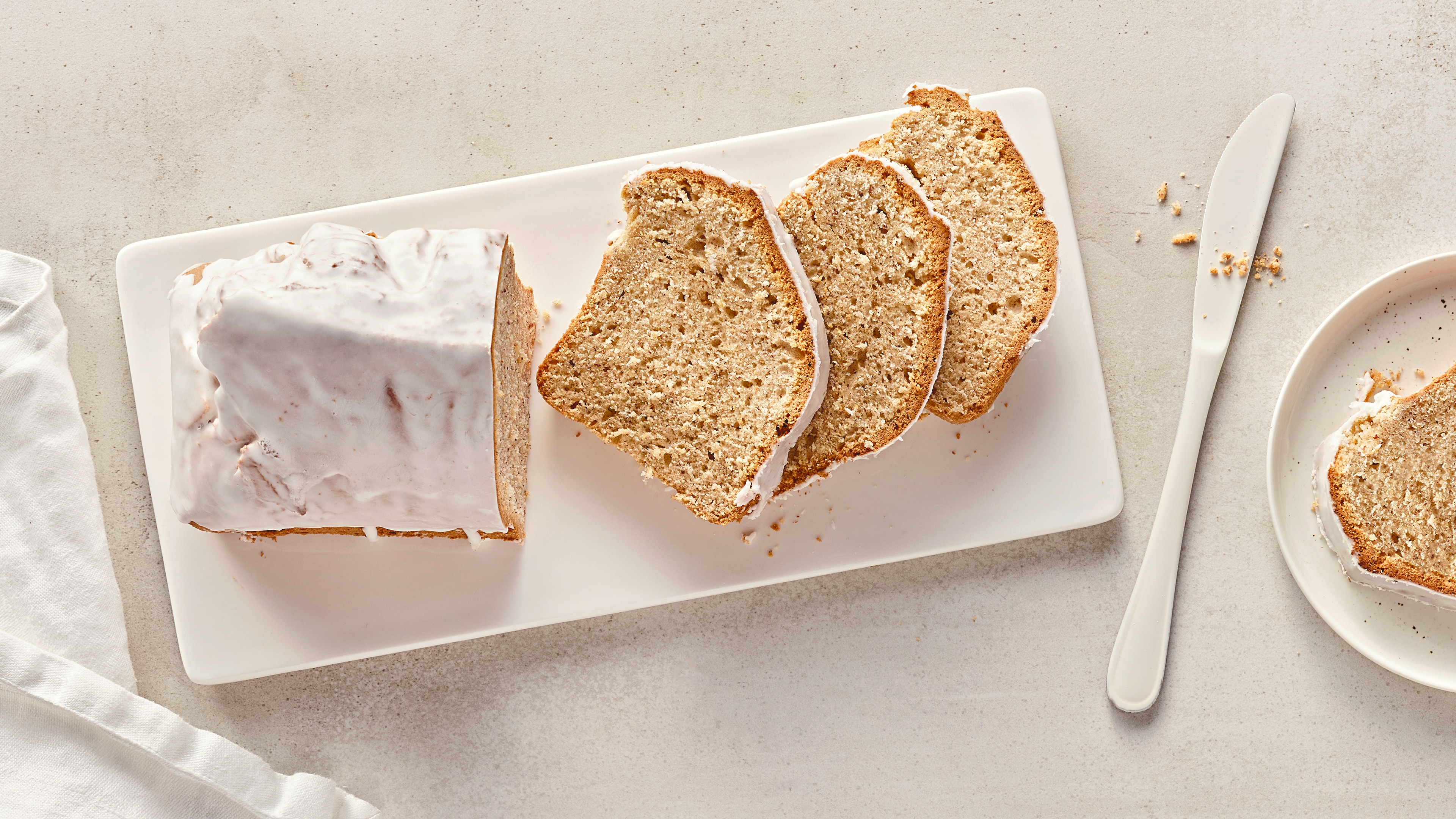 Rezept für Kuchen aus der Heißluftfritteuse Ein heller, fluffiger Kuchen, überzogen mit einer weißen Zuckerglasur, auf einer weißen Keramikplatte