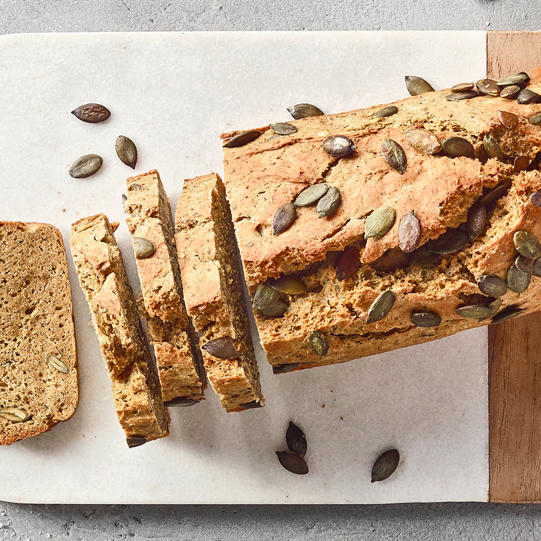 Ein Brett mit einem aufgeschnittenen Laib Brot, bestreut mit grünen Kürbiskernen.