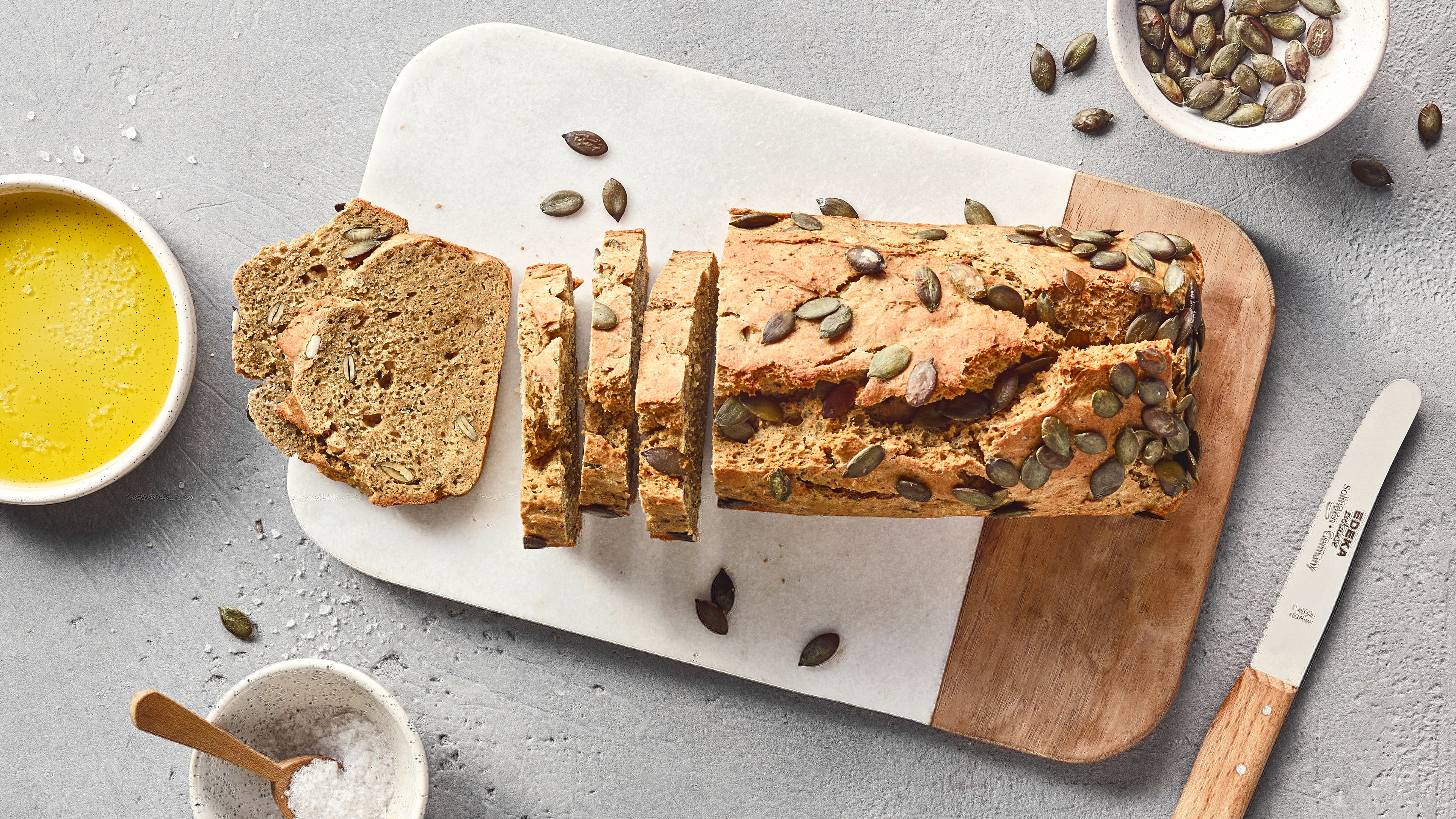 Ein Brett mit einem aufgeschnittenen Laib Brot, bestreut mit grünen Kürbiskernen.