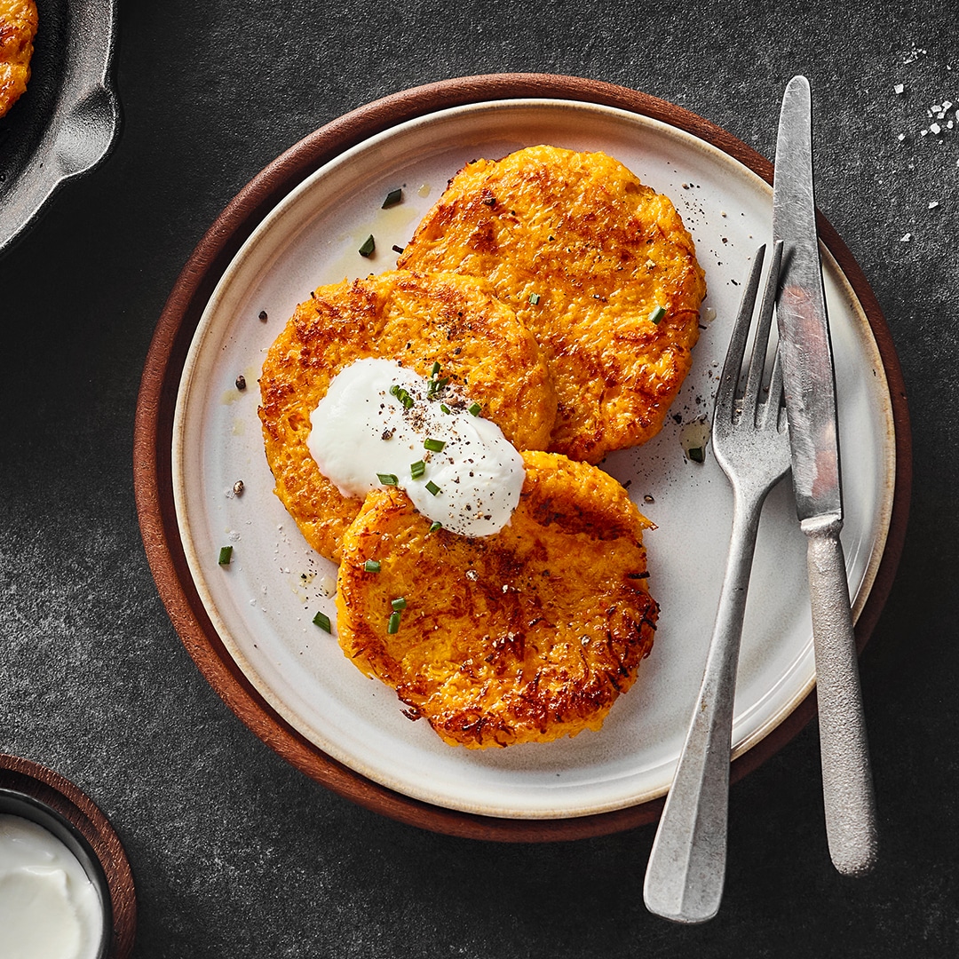 Knusprig angebratene, orangene Puffer, getoppt mit einer weißen Sauce auf einem runden Teller