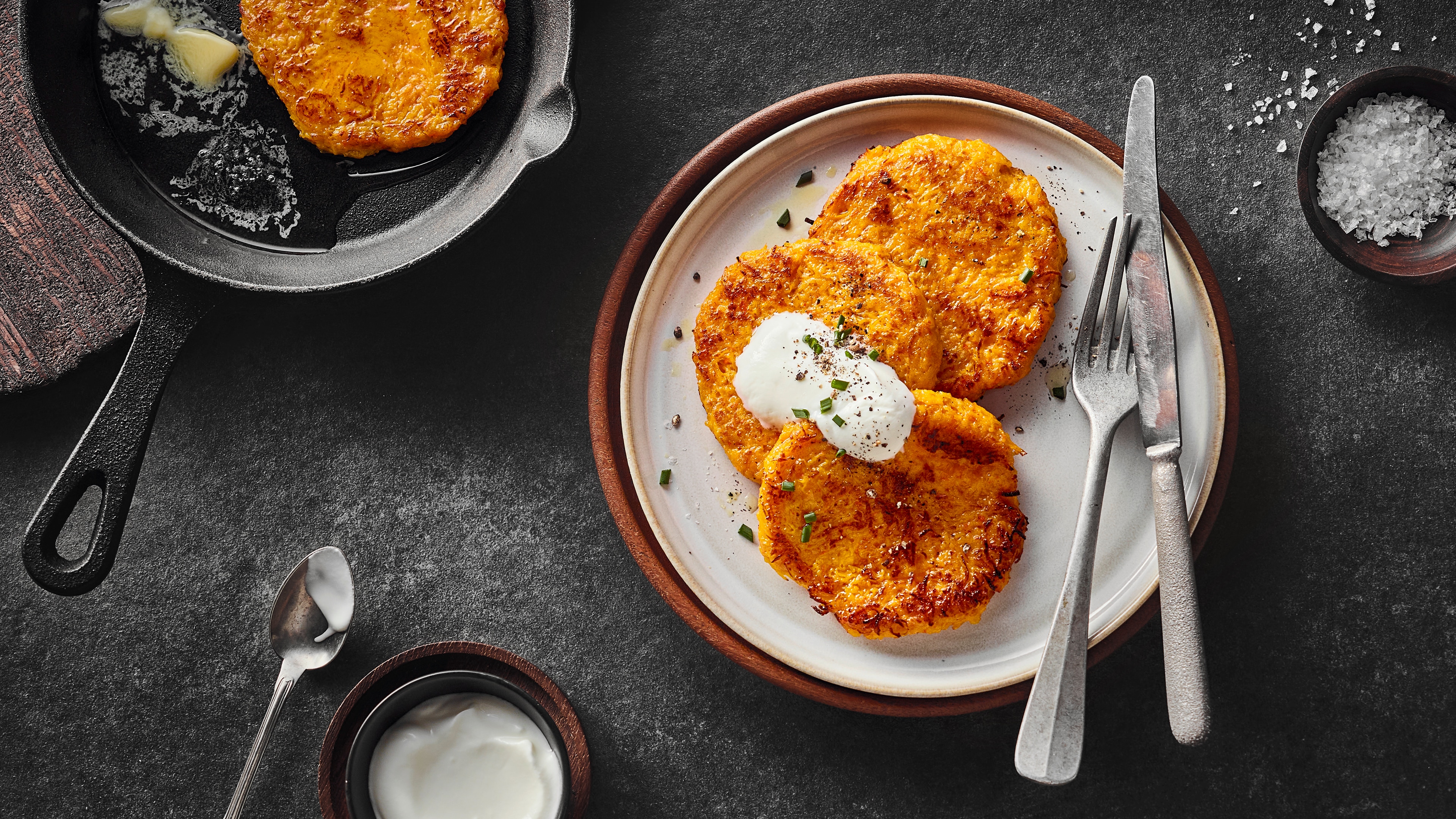 Rezept für Kürbispuffer Knusprig angebratene, orangene Puffer, getoppt mit einer weißen Sauce auf einem runden Teller