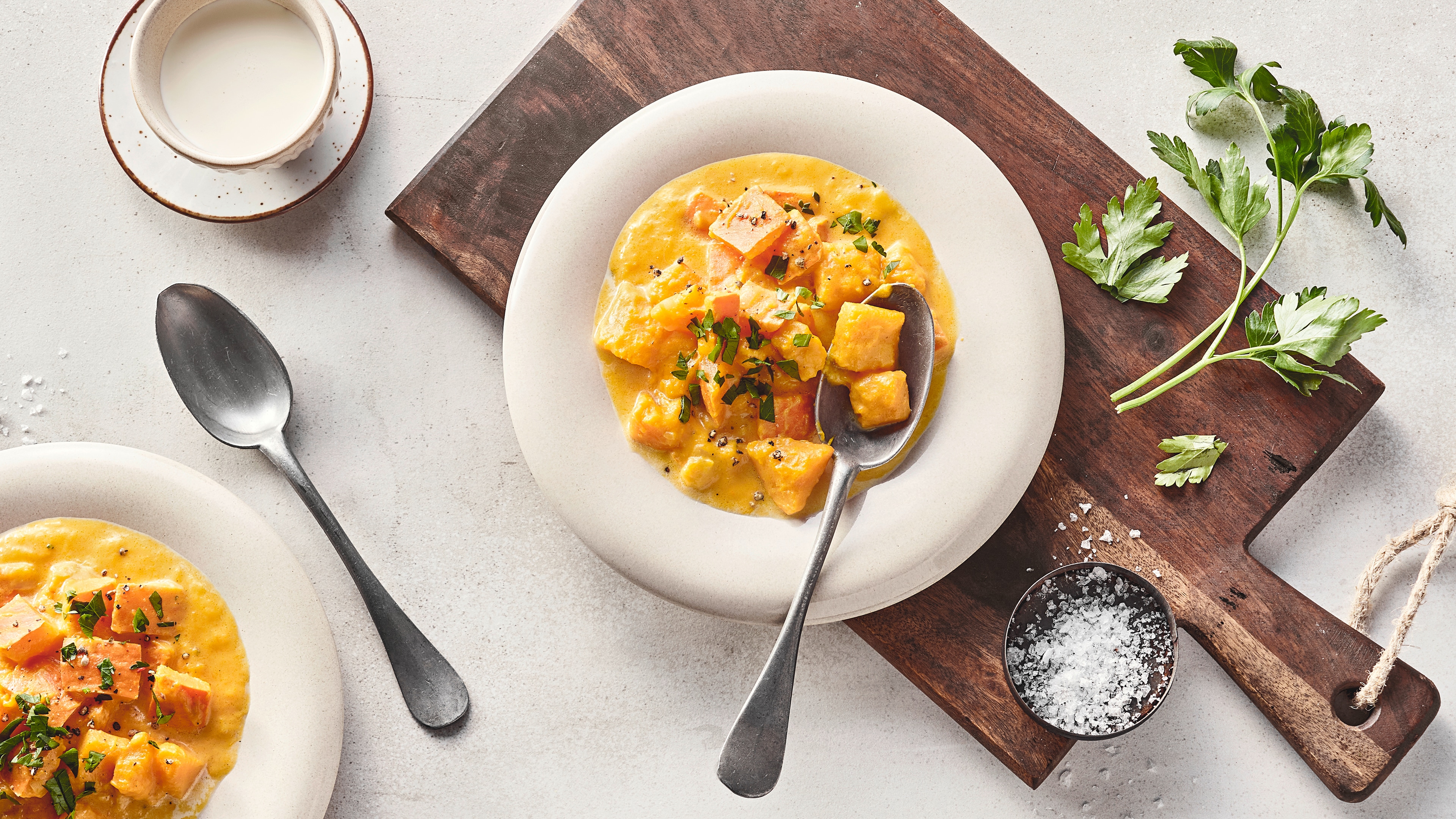 Rezept für Kürbisragout Homogene Kürbis-Creme und Kürbis-Würfel, getoppt mit frischer Petersilie, auf einem Teller auf einem rustikalen Holzbrett