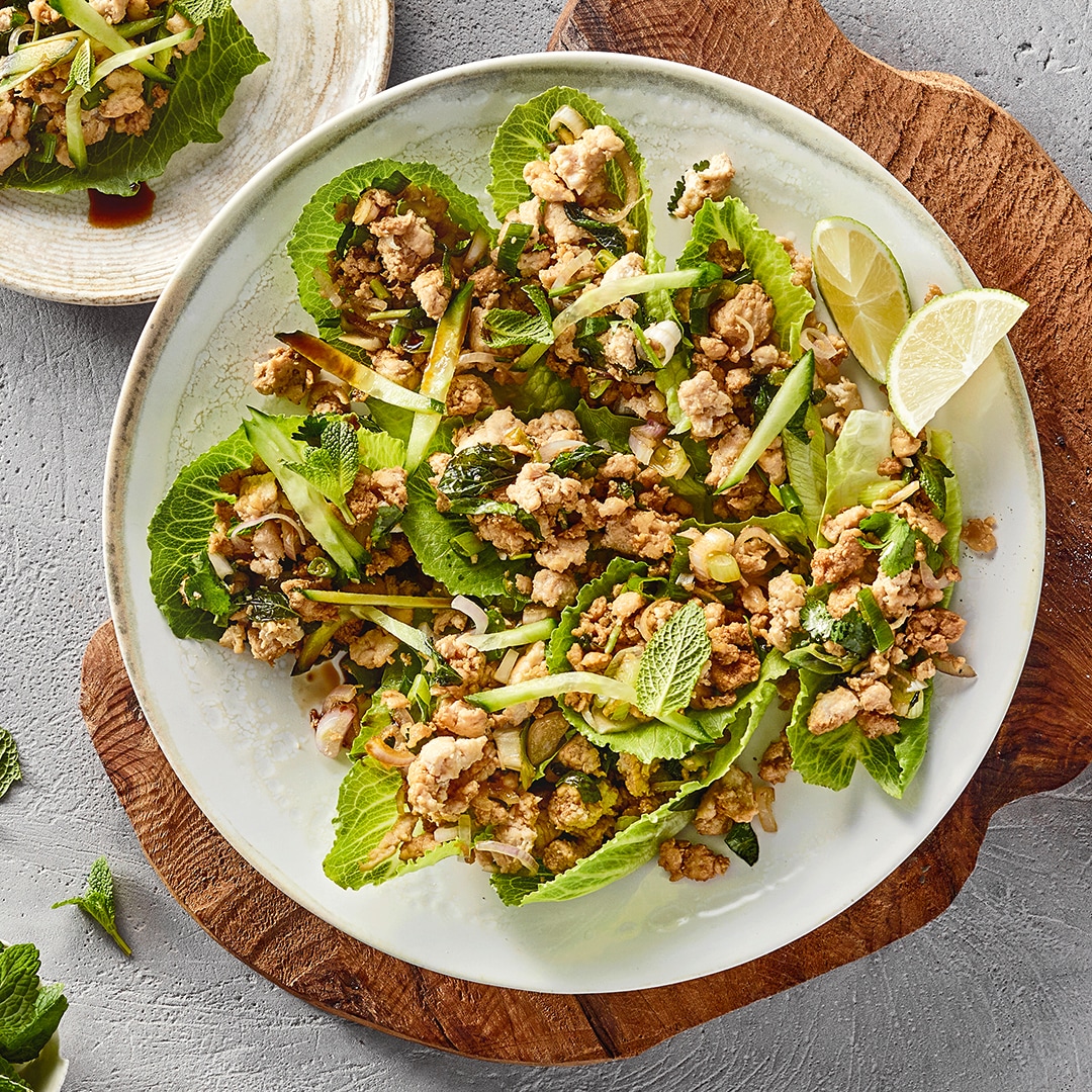 Salat aus grünen Blättern und krümeligem Fleisch auf weißem Teller auf Holzbrett