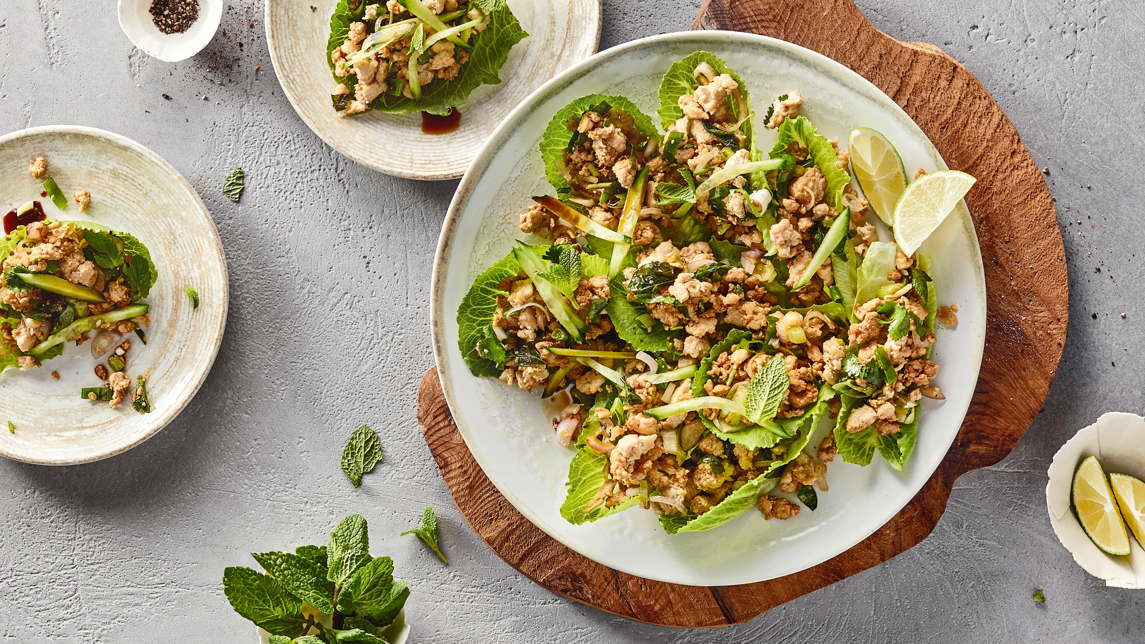 Salat aus grünen Blättern und krümeligem Fleisch auf weißem Teller auf Holzbrett