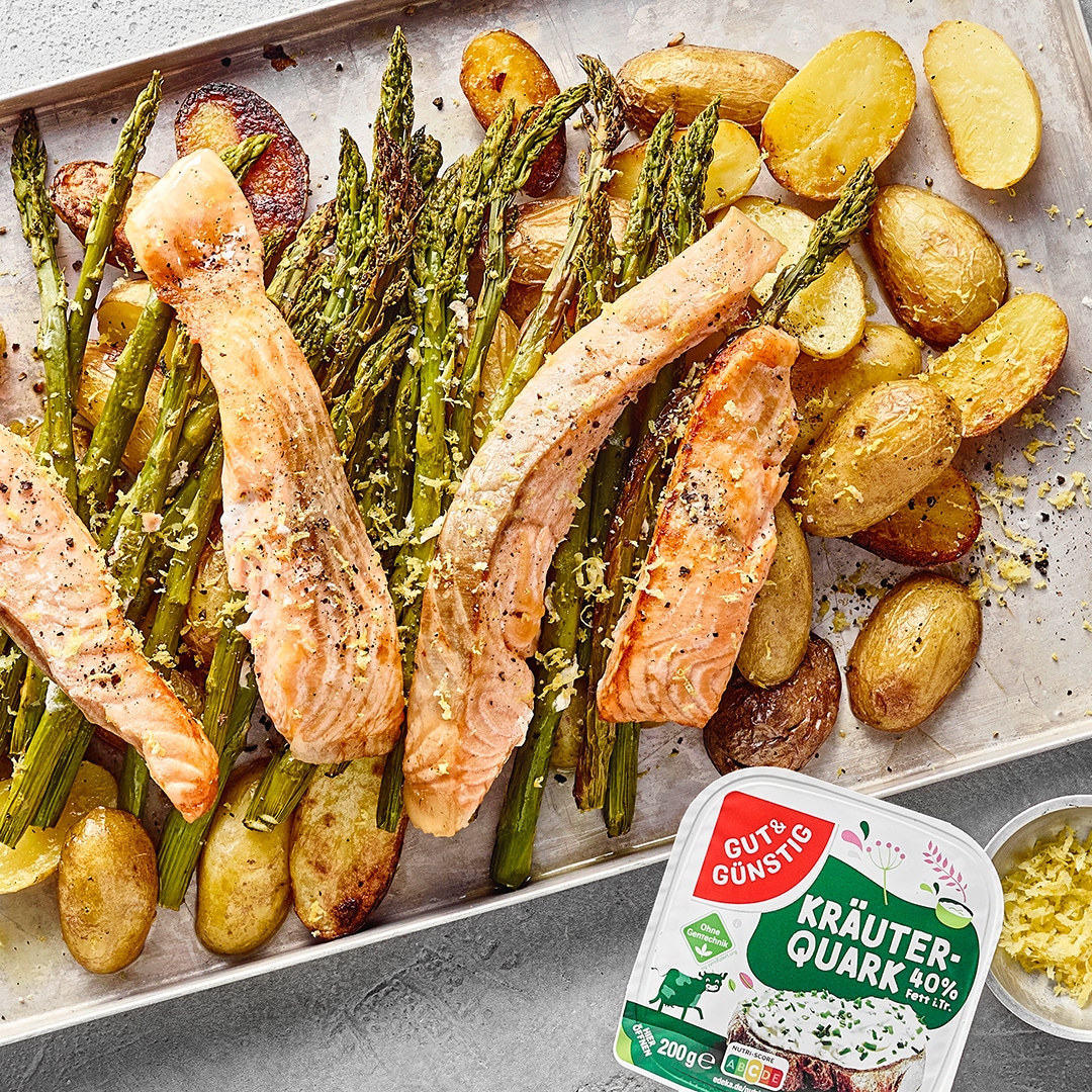 Ofenblech mit Lachsfilets, umgeben von goldbraunen Kartoffelhälften und grünem Spargel. Daneben GUT&GüNSTIG Kräuterquark.