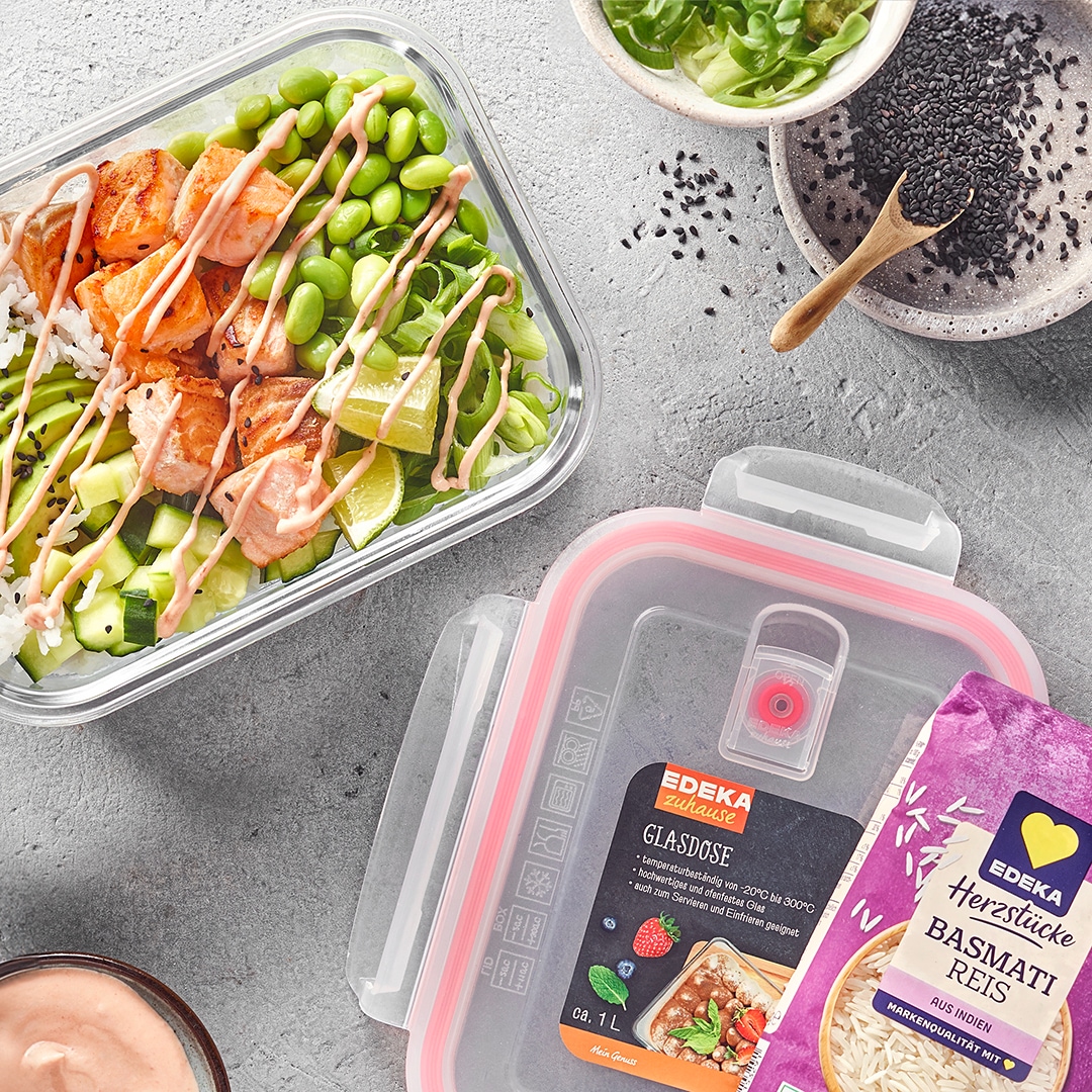 Meal-Prep-Box mit Basmatireis, Avocado, Edamame und gebratenen Hähnchenstücken, daneben eine Packung EDEKA Herzstücke Basmatireis und EDEKA Zuhause Glasdose.