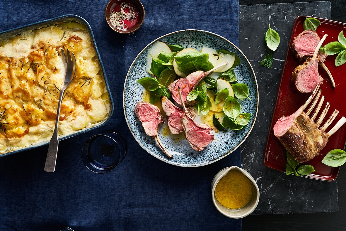 Rezept für Lammkarree mit Kartoffelgratin und Spinatsalat Ein Teller mit vier Lammkoteletts, Blattspinat und Zucchinischeiben in einer hellen Soße