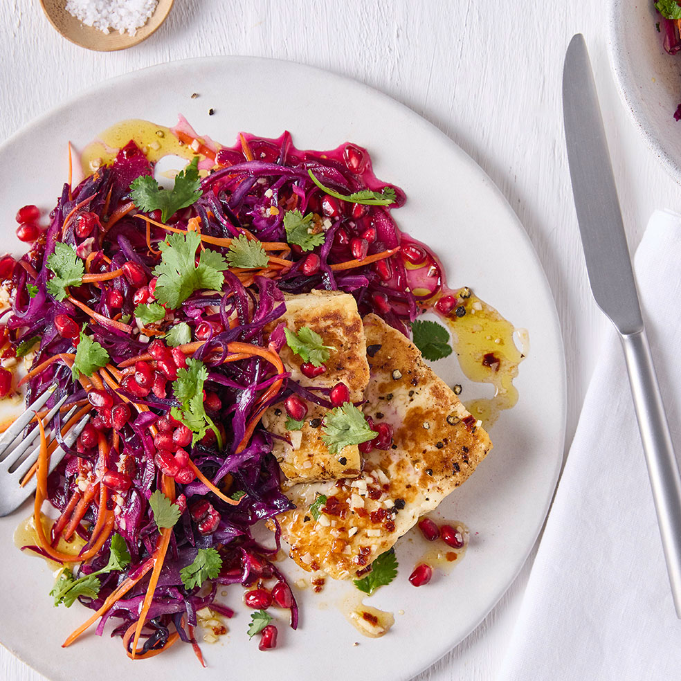 Ein Teller mit gebratenem Halloumi, dazu ein bunter Salat aus Rotkohl, Karottenstreifen, Granatapfelkernen und Kräutern.