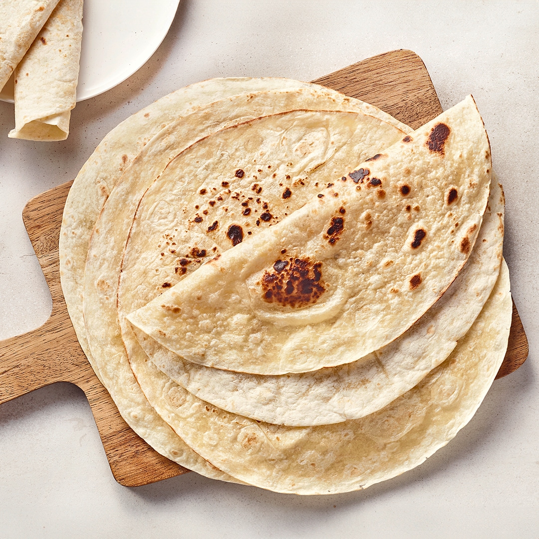 Ein Holzbrett mit mehreren hellen, dünnen Fladen, teils gefaltet und mit braunen Backflecken.