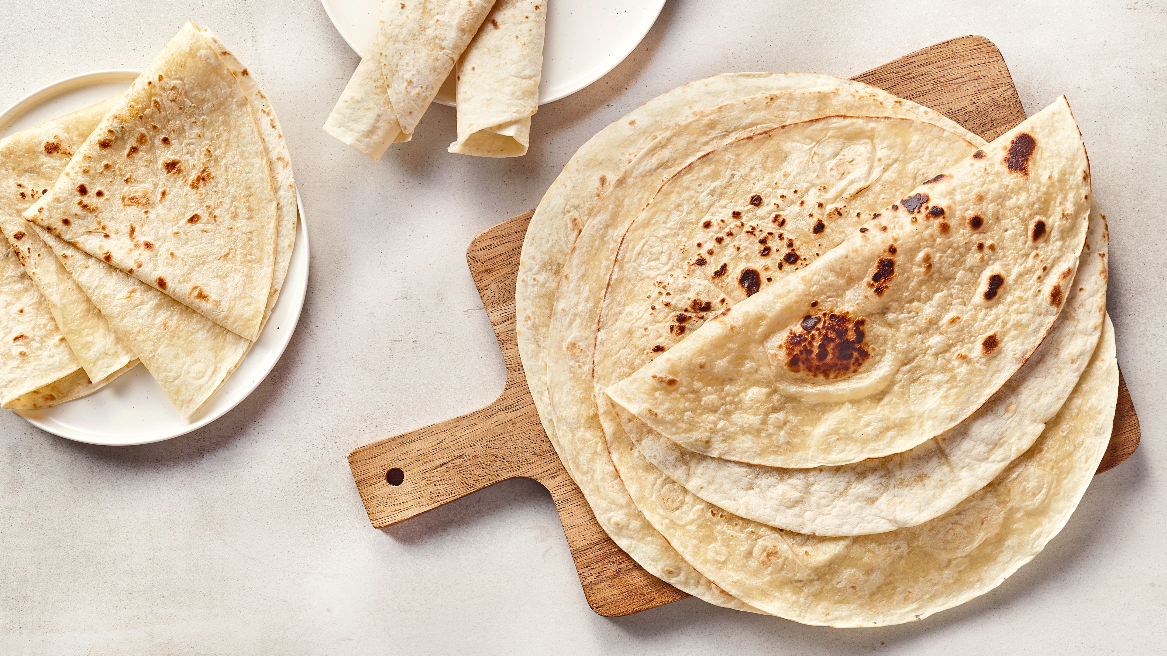 Ein Holzbrett mit mehreren hellen, dünnen Fladen, teils gefaltet und mit braunen Backflecken.