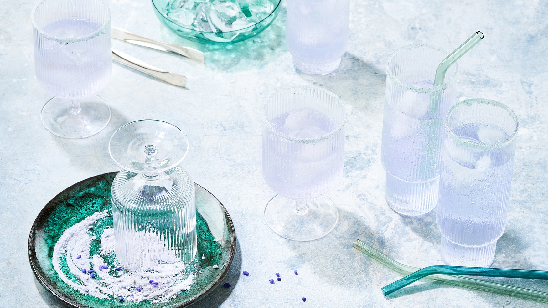 Rezept für Lavendel Spritz Mit hellblau-violetter Flüssigkeit und Eiswürfeln gefüllte Gläser