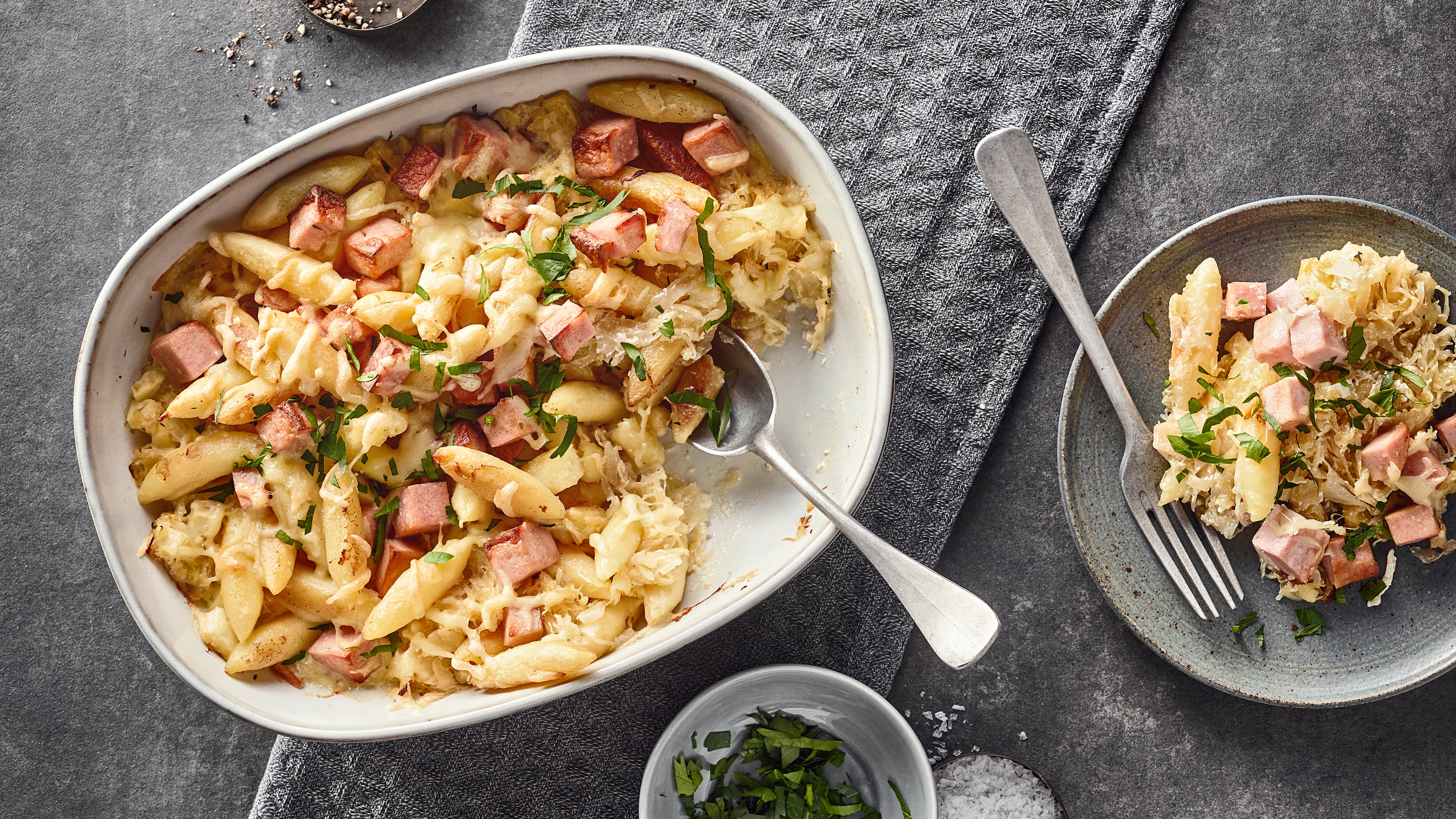 Rezept für Leberkäse-Auflauf Eine Auflaufform mit überbackenen Schupfnudeln und Leberkäse-Würfeln, getoppt mit frisch gehackter Petersilie