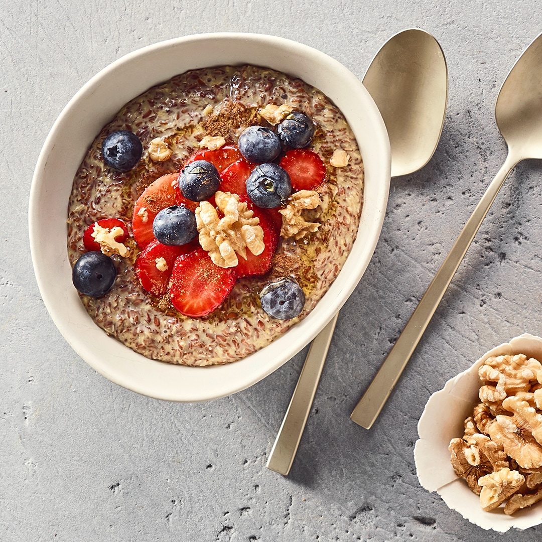 Eine Schüssel mit Leinsamen-Pudding, darauf rote Erdbeerscheiben, ganze blaue Heidelbeeren und grobe Stücke heller Walnüsse.