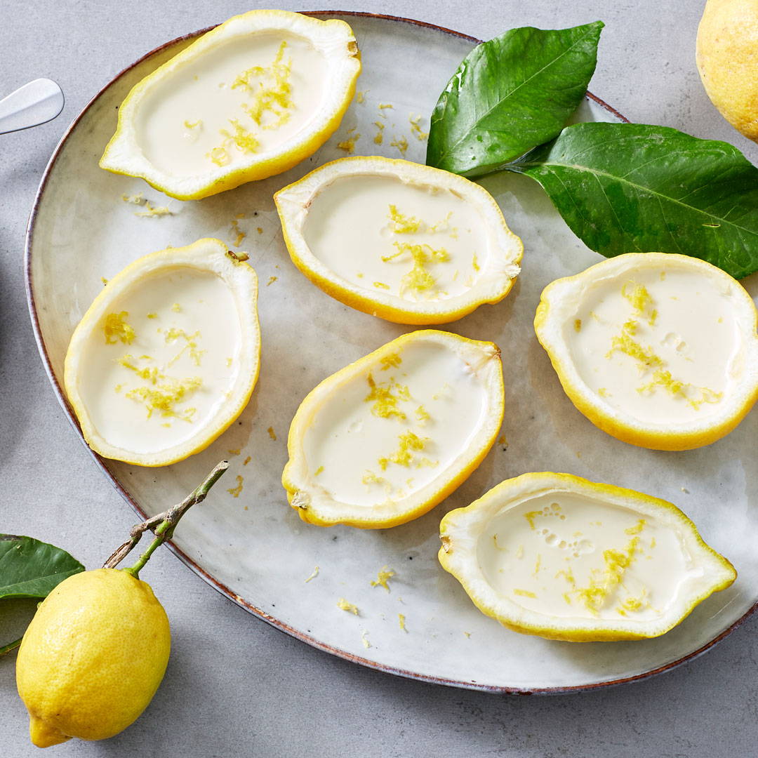 Zitronenhälften,  gefüllt mit heller Creme, getoppt mit geriebener Zitronenschale, auf einem ovalen Teller