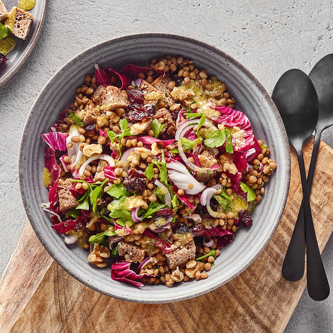 Große Schale mit einem Salat aus Linsen, Brotstücken, roten Salatblättern und Zwiebeln