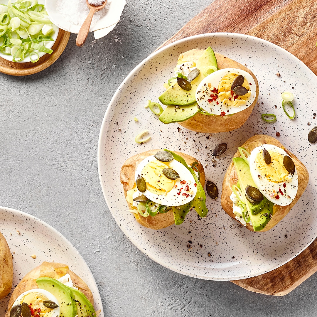 Ofenkartoffeln mit Avocado, Ei, Frühlingszwiebeln und Kürbiskernen auf einem Teller.