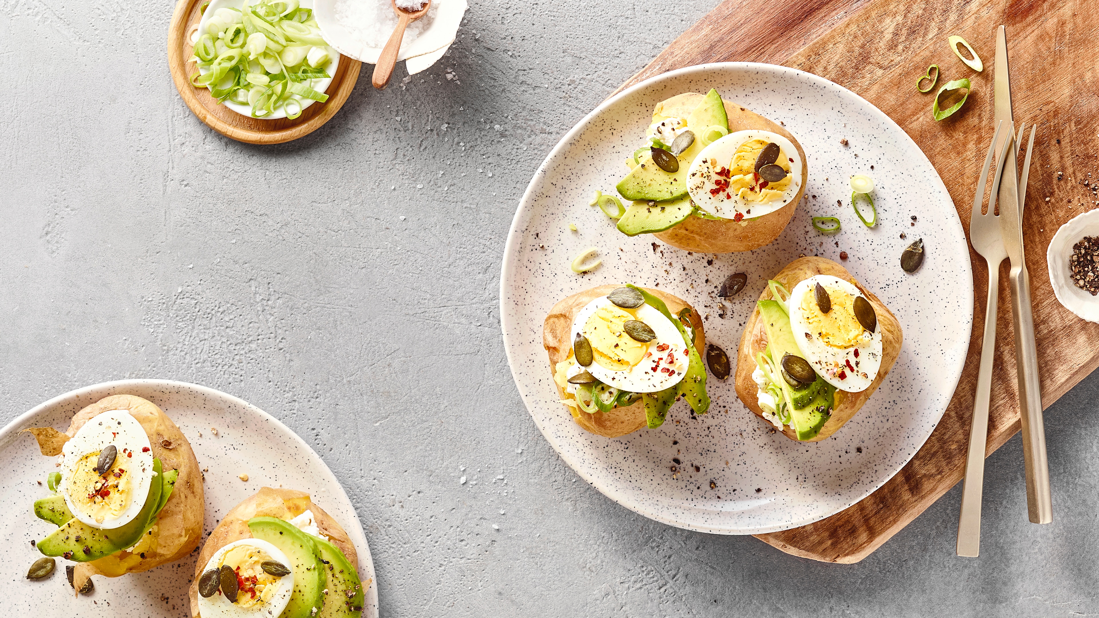 Ofenkartoffeln mit Avocado, Ei, Frühlingszwiebeln und Kürbiskernen auf einem Teller.