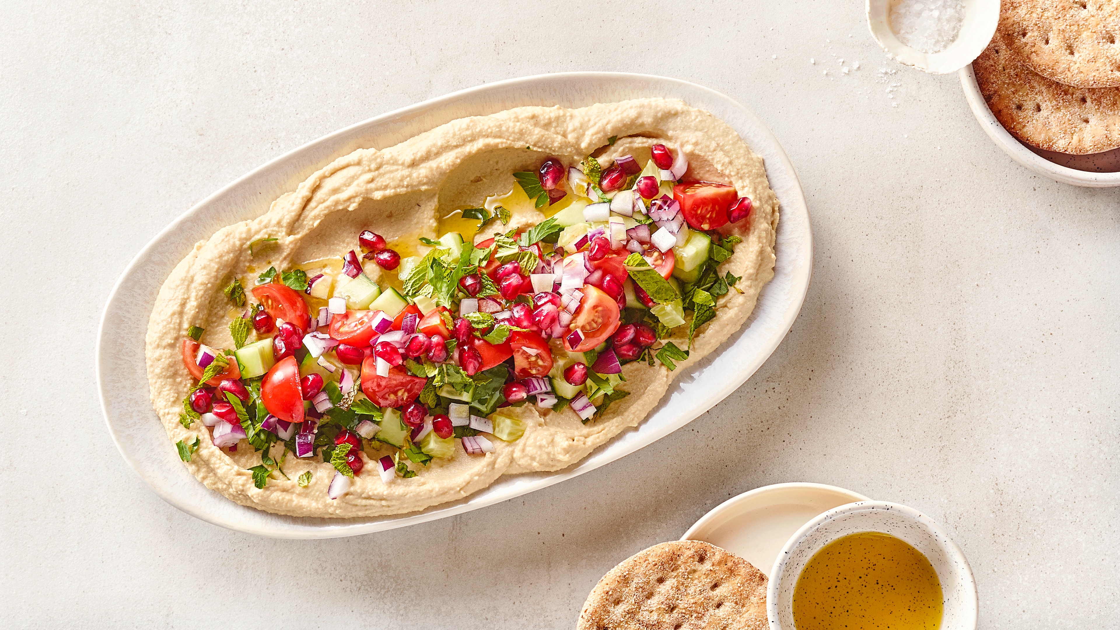 Große Platte mit Hummus und darauf Tomatenhälften, Gurkenscheiben, Granatapfelkernen und Zwiebelstückchen