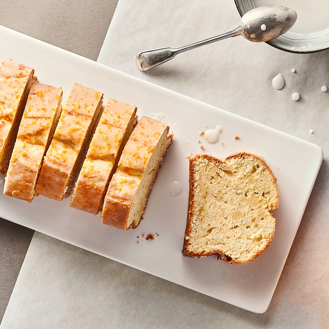 Ein paar Stücke saftiger Kastenkuchen, überzogen mit Zuckerguss und garniert mit Zitronenabrieb, auf einem länglichen Teller