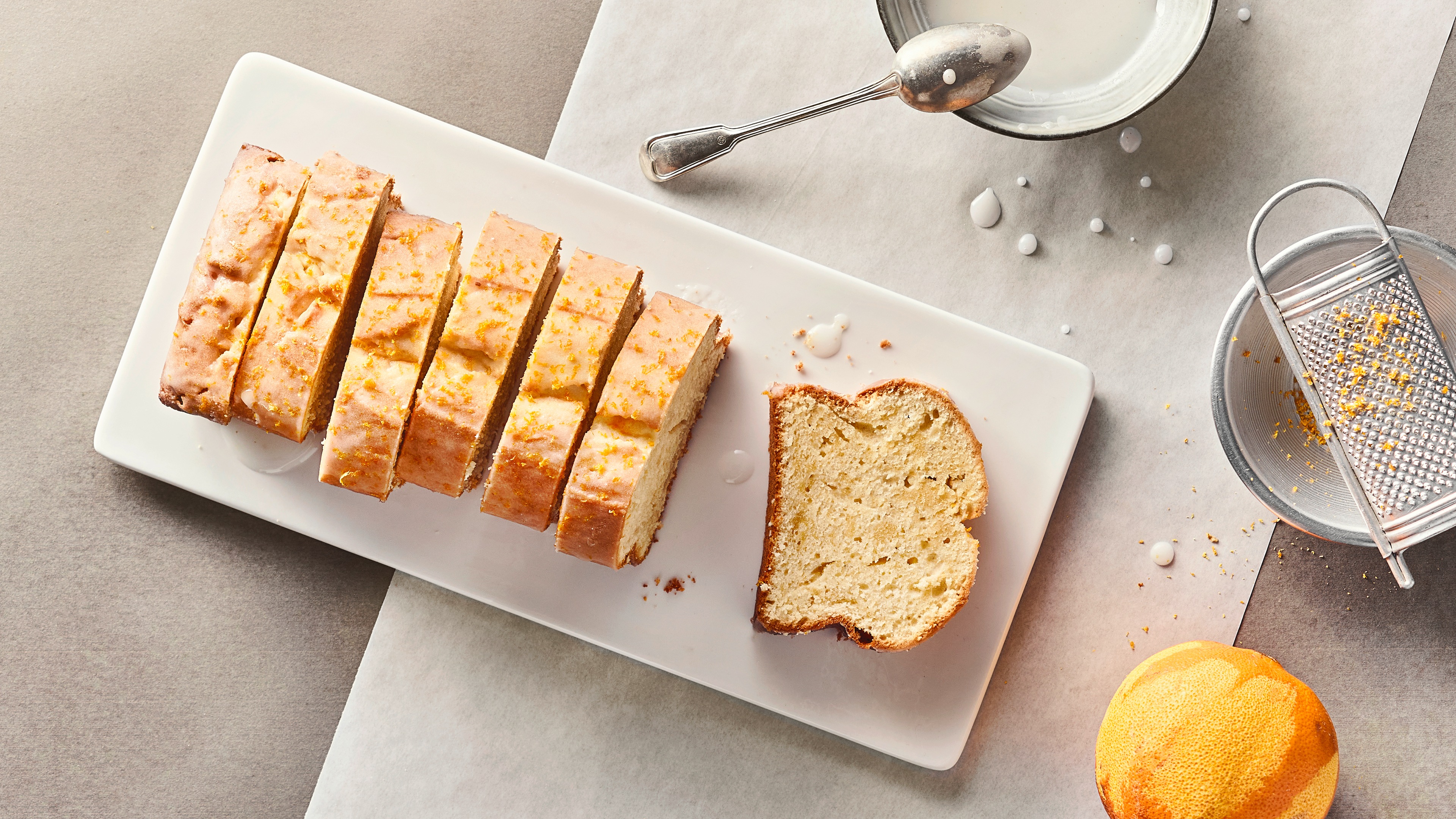 Ein paar Stücke saftiger Kastenkuchen, überzogen mit Zuckerguss und garniert mit Zitronenabrieb, auf einem länglichen Teller