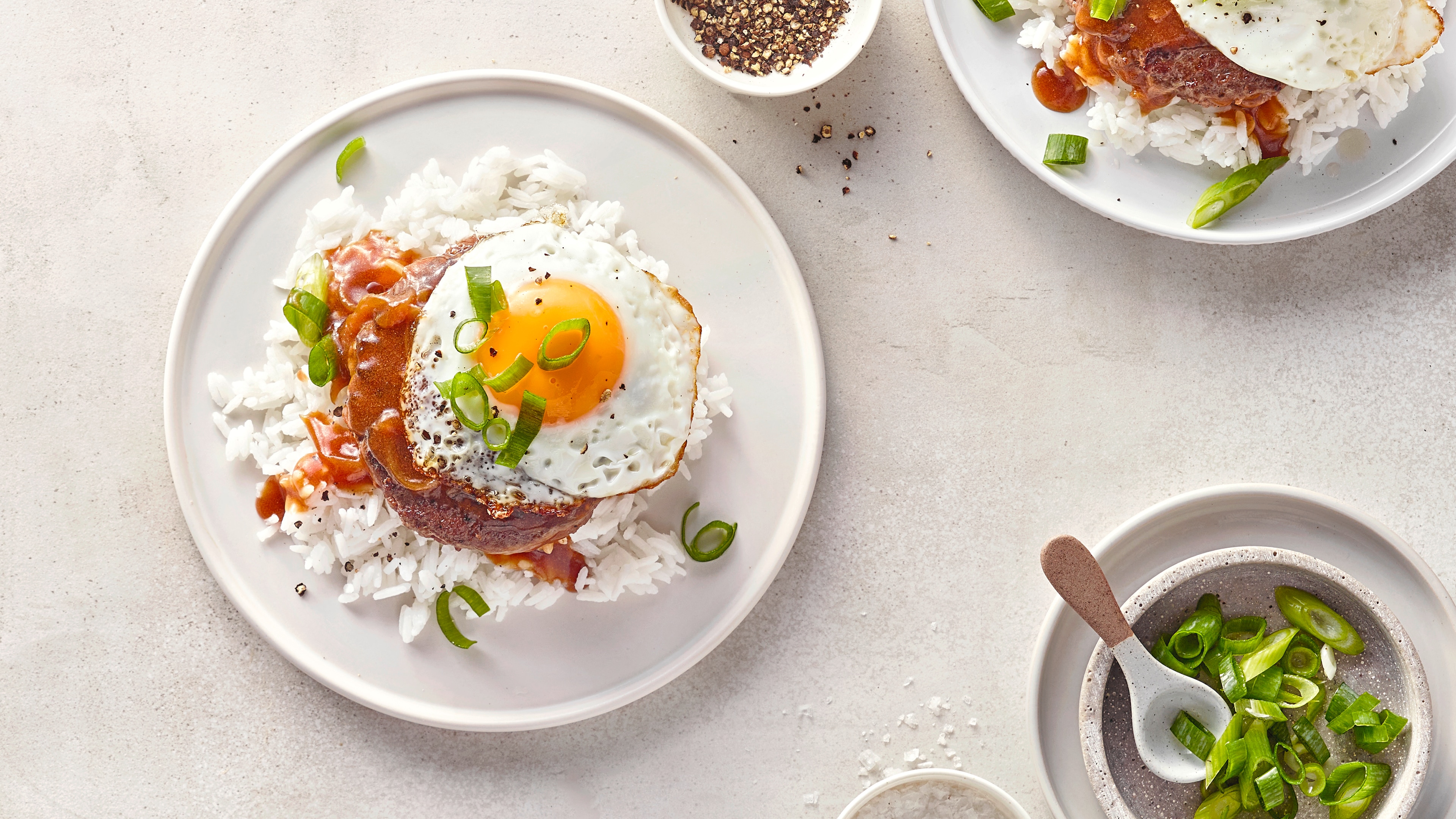 Rezept für Loco Moco Ein Teller mit weißem Reis, einem Hamburgerpatty, brauner Soße, einem Spiegelei und geschnittenen Frühlingszwiebeln
