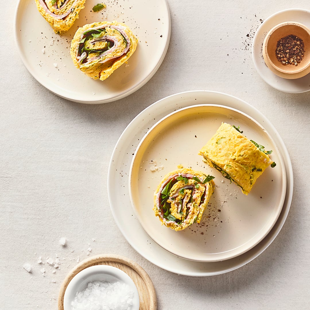 Runde Teller mit geschnittenen Omlette-Rollen mit Schinken und Gemüse