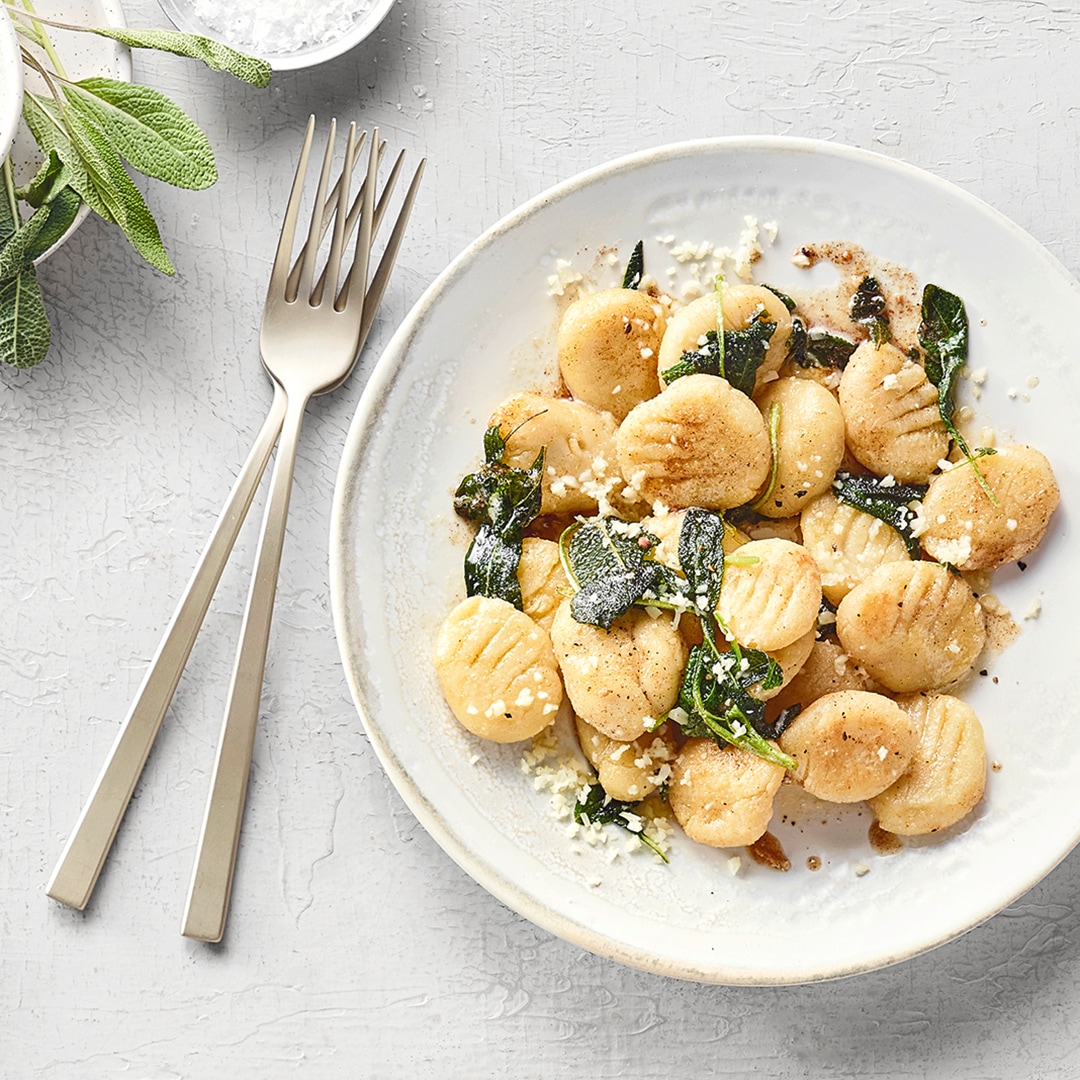 Flache Gnocchi mit Käse und grünen Salbeiblättern auf einem Teller