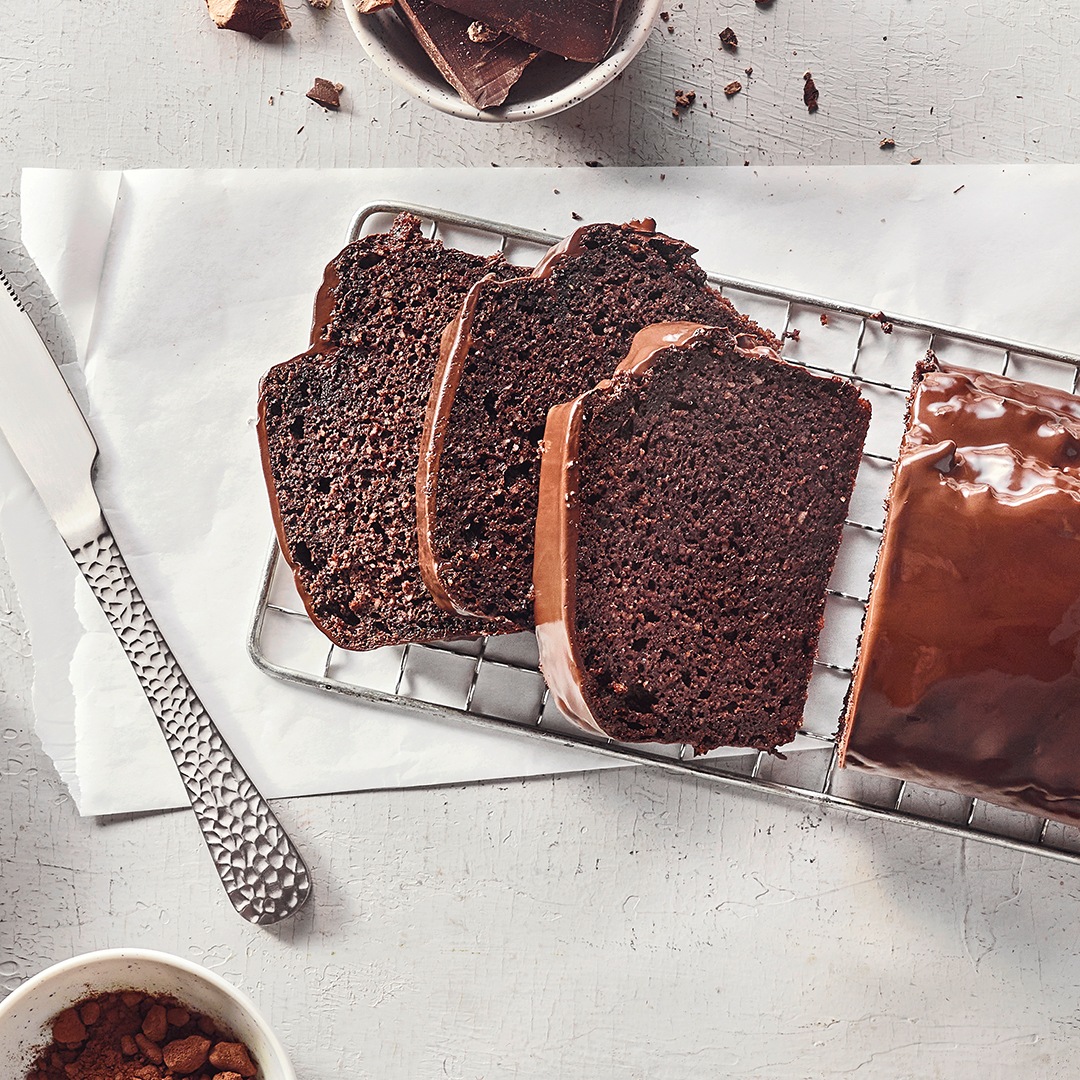 Ein Gitter mit Scheiben dunklem Kuchen und einem ganzen Stück, alle mit glatter brauner Glasur überzogen.