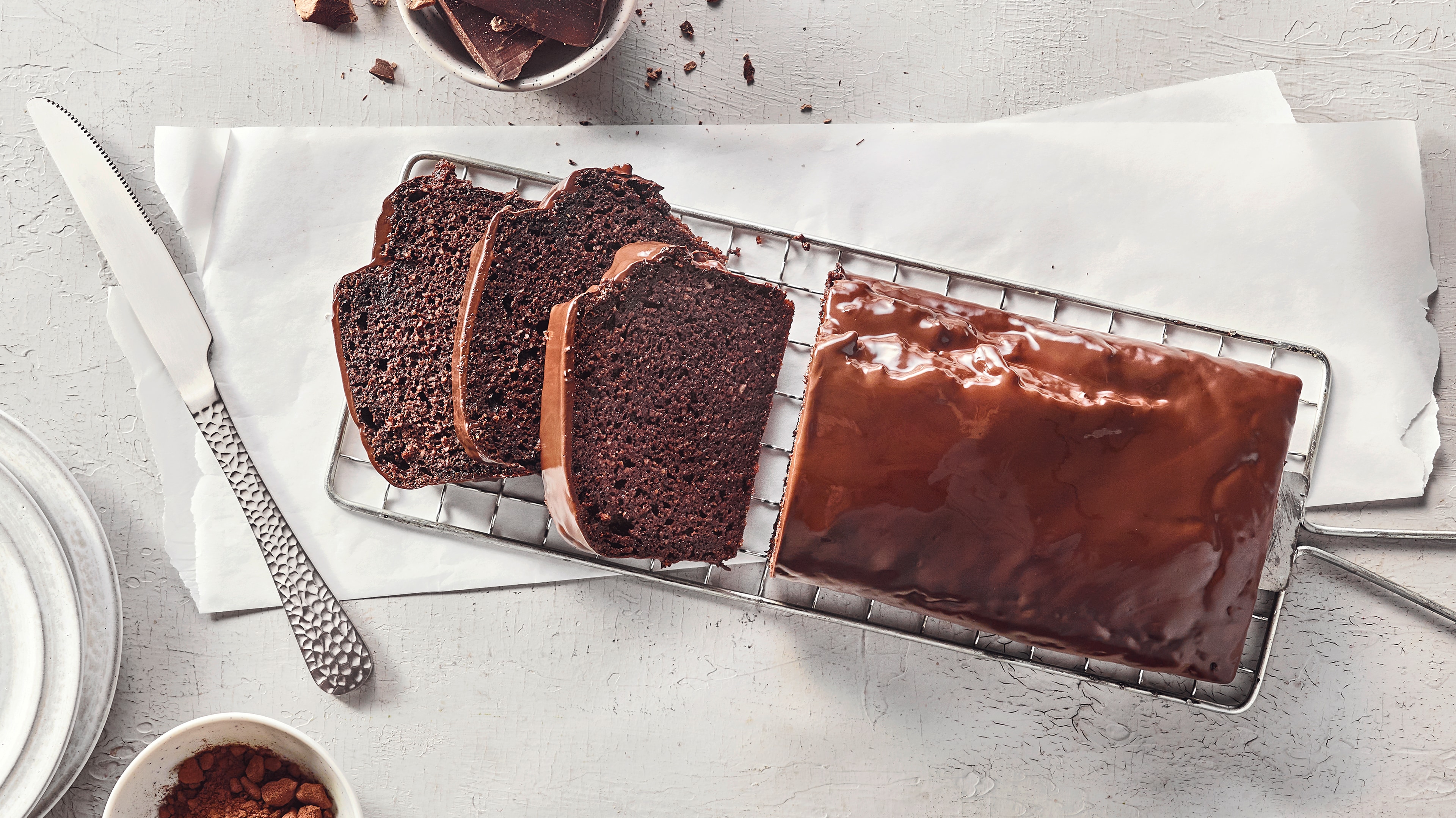Ein Gitter mit Scheiben dunklem Kuchen und einem ganzen Stück, alle mit glatter brauner Glasur überzogen.