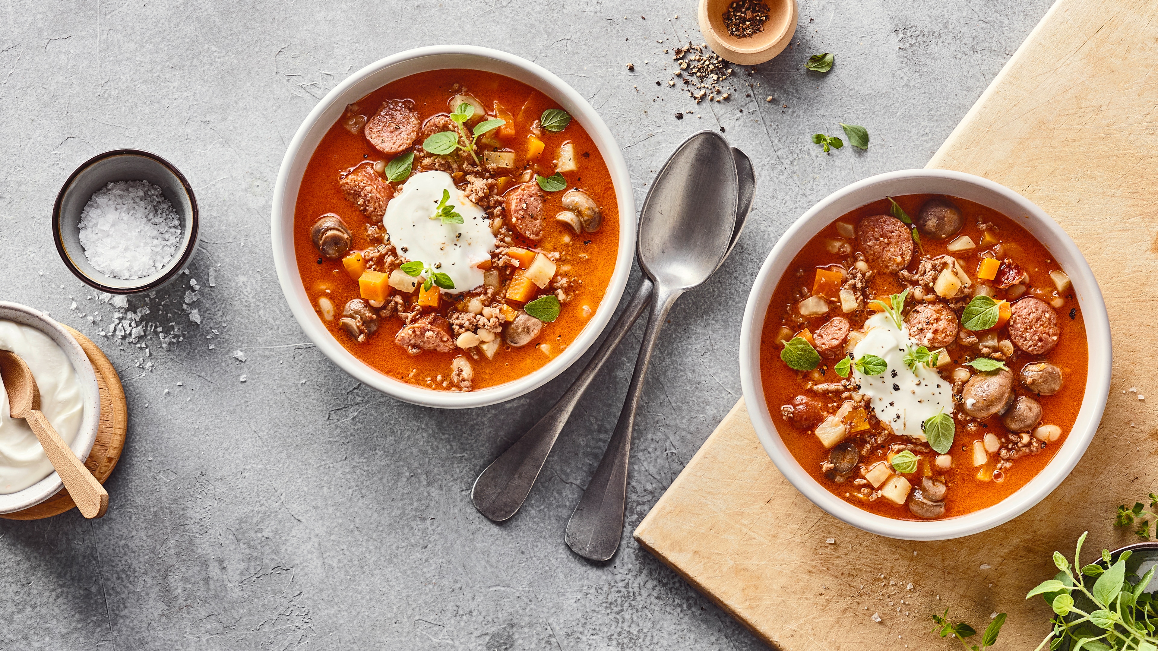 Rezept für Lumpensuppe Teller mit hellbrauner Suppe mit Wurststückchen, Champignons und Möhrenwürfeln, getoppt mit einem Klecks weißer Creme