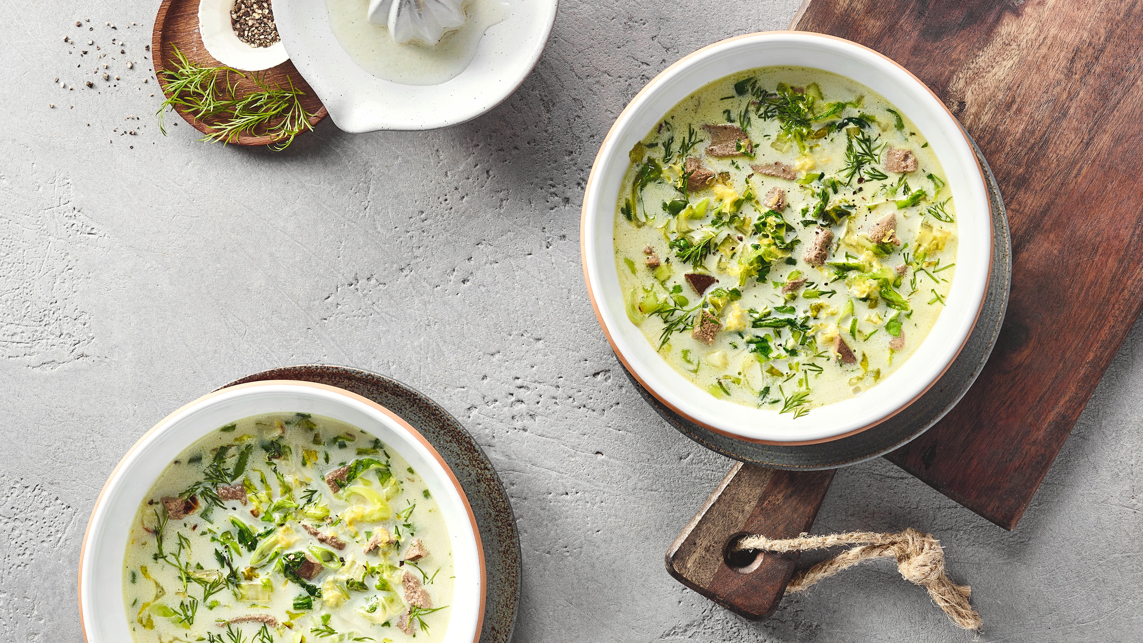 Ein Teller mit grüner cremiger Suppe, darin Fleischstücke, Kohlstreifen und Dill.