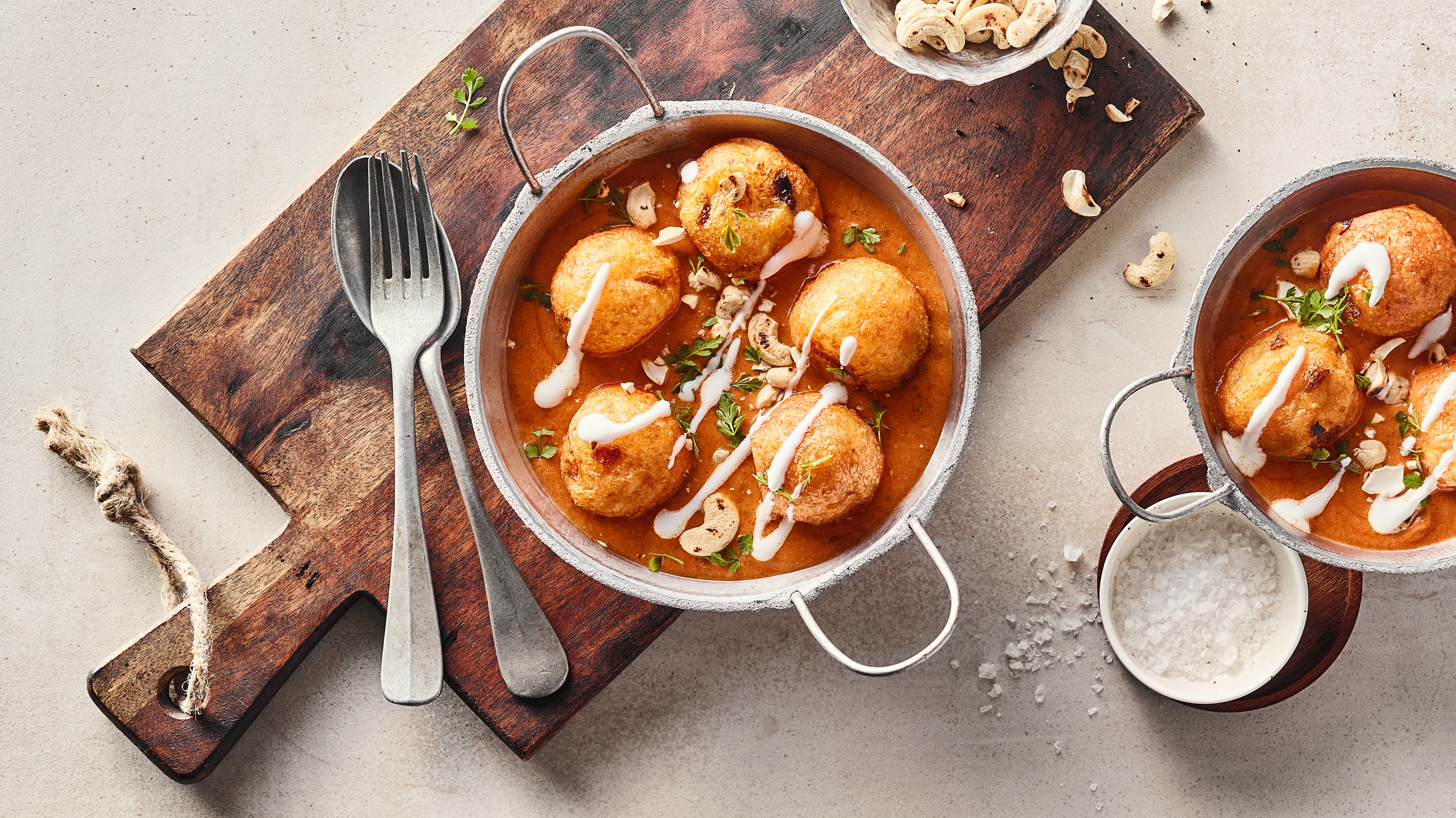 Rezept für indische Malai Kofta Ein gusseiserner Topf mit krossen Teigkugeln in einer hellbraunen, klaren Sauce, garniert mit Sahne und gerösteten Cashews