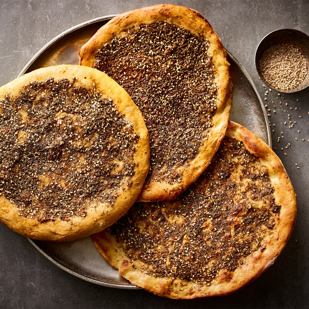 Telllergroße, gelbgold gebackene Fladenbrote mit verschiedenen Gewürzen wie eine Pizza belegt ist, auf einem Metall-Tablett
