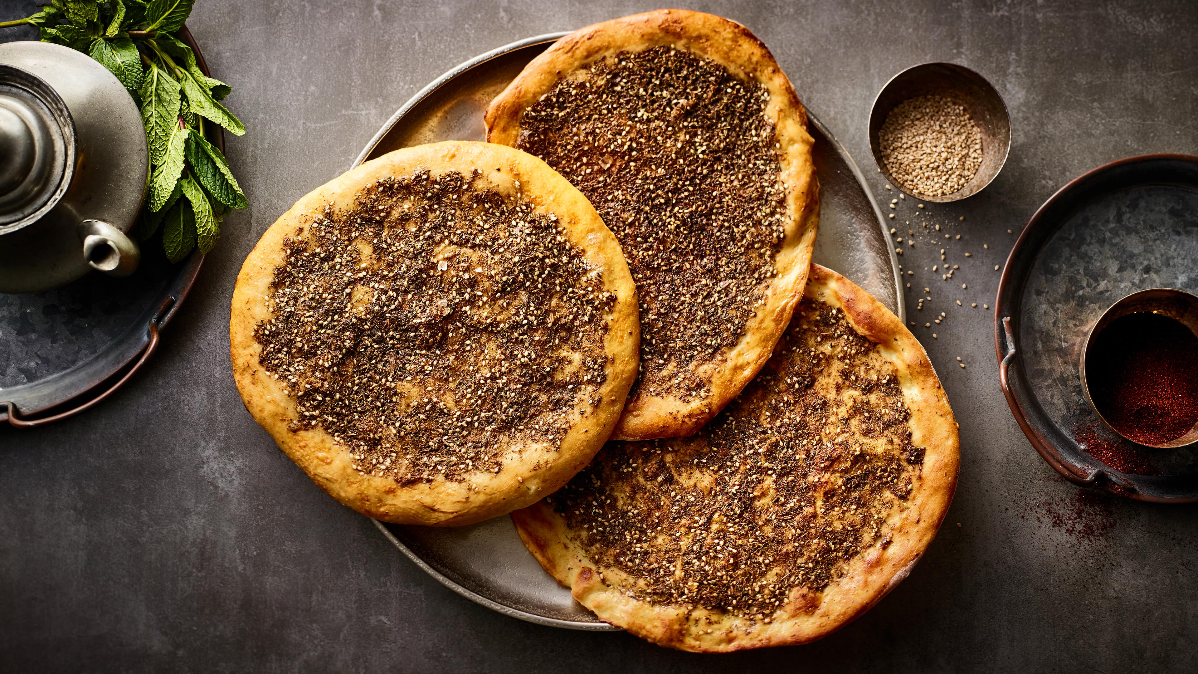 Rezept für arabische Manakish Telllergroße, gelbgold gebackene Fladenbrote mit verschiedenen Gewürzen wie eine Pizza belegt ist, auf einem Metall-Tablett