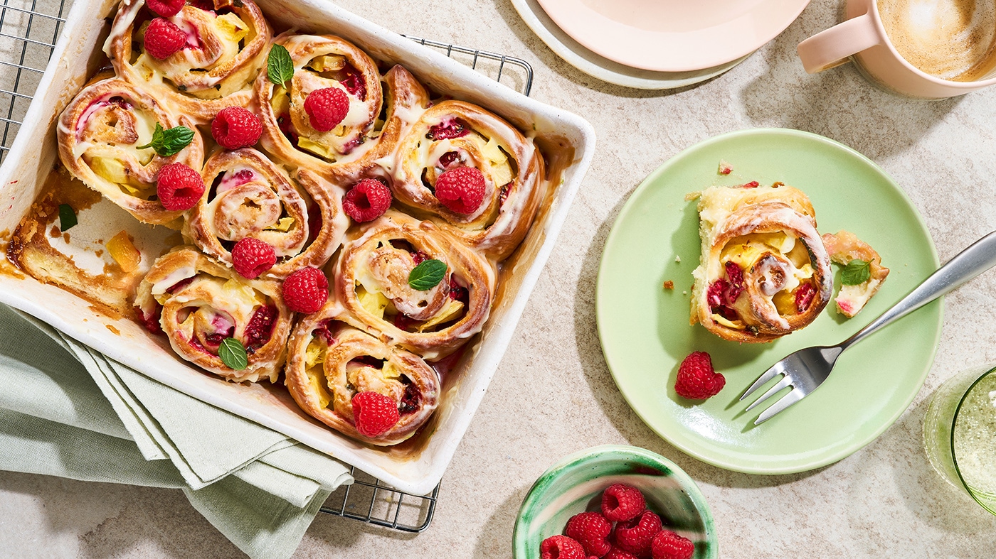 Auflaufform mit in Schneckenform gebackenen Teigstücken, dazu Himbeeren