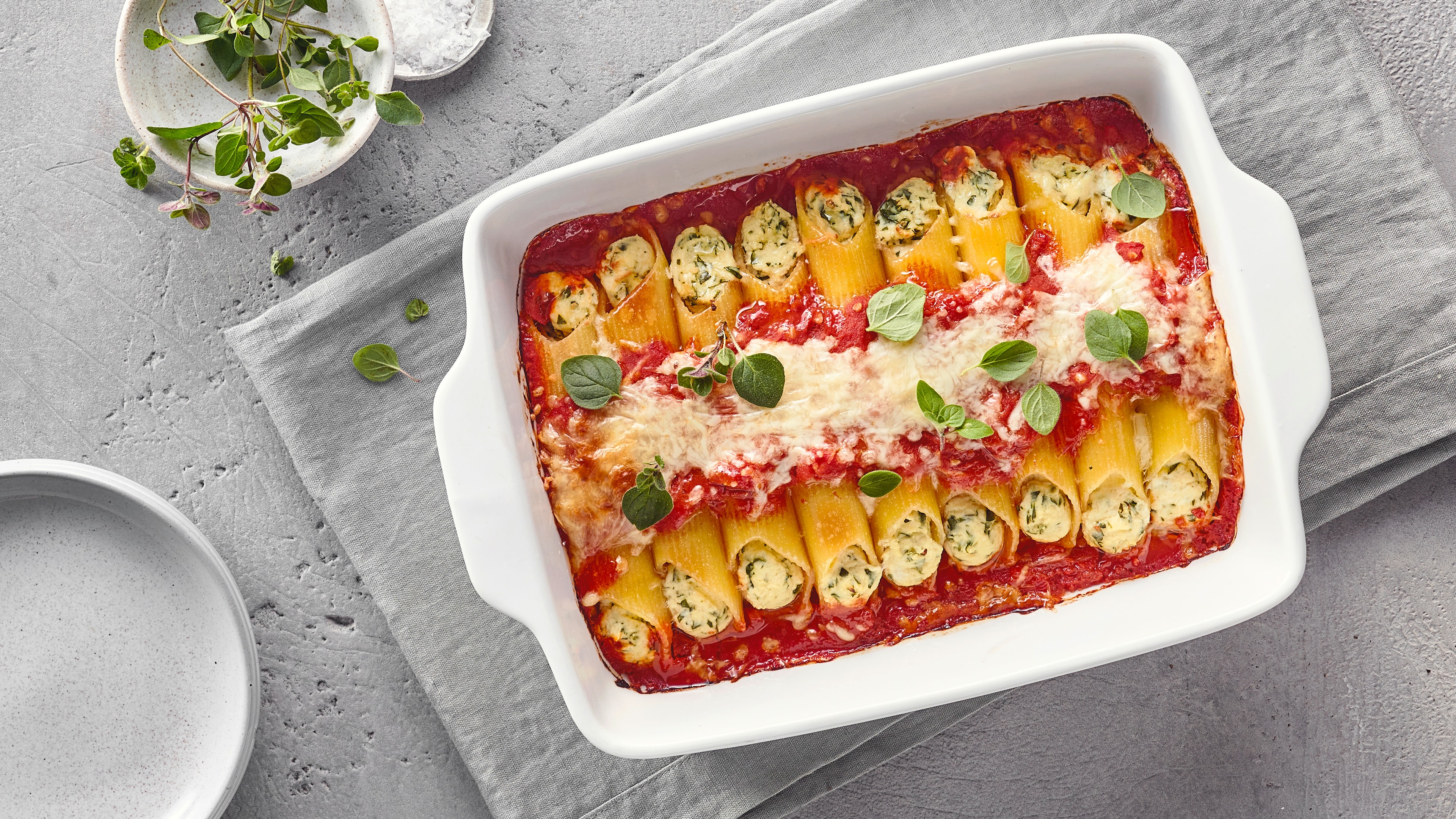 Rezept für Manicotti Eine Form mit gebackenen Nudelrollen, gefüllt mit Ricotta und Kräutern, bedeckt mit Tomatensoße, Käse und frischem Basilikum