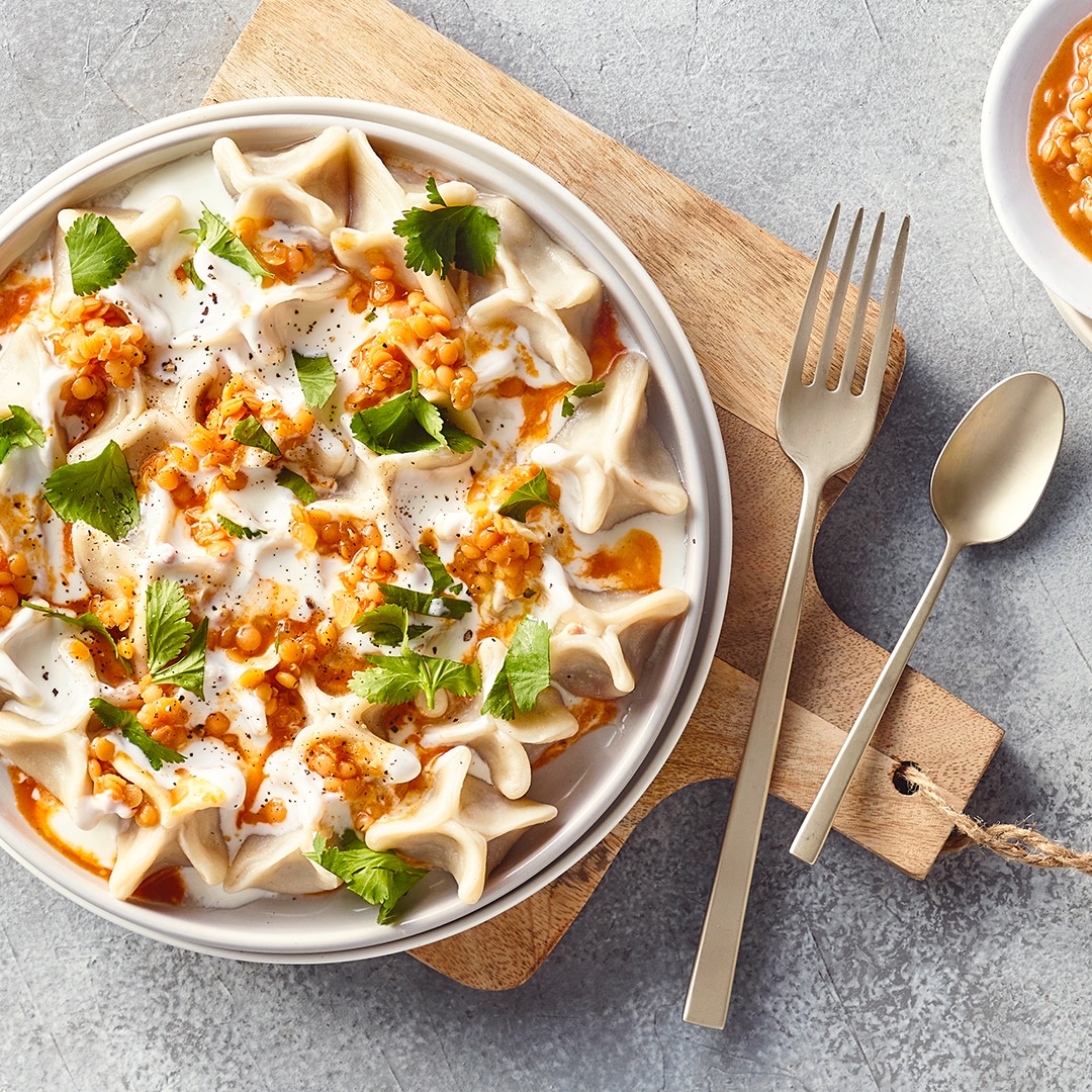 Ein Teller mit gefüllten Teigtaschen, bedeckt mit weißer Sauce, garniert mit gehackten Kräutern und kleinen Körnern