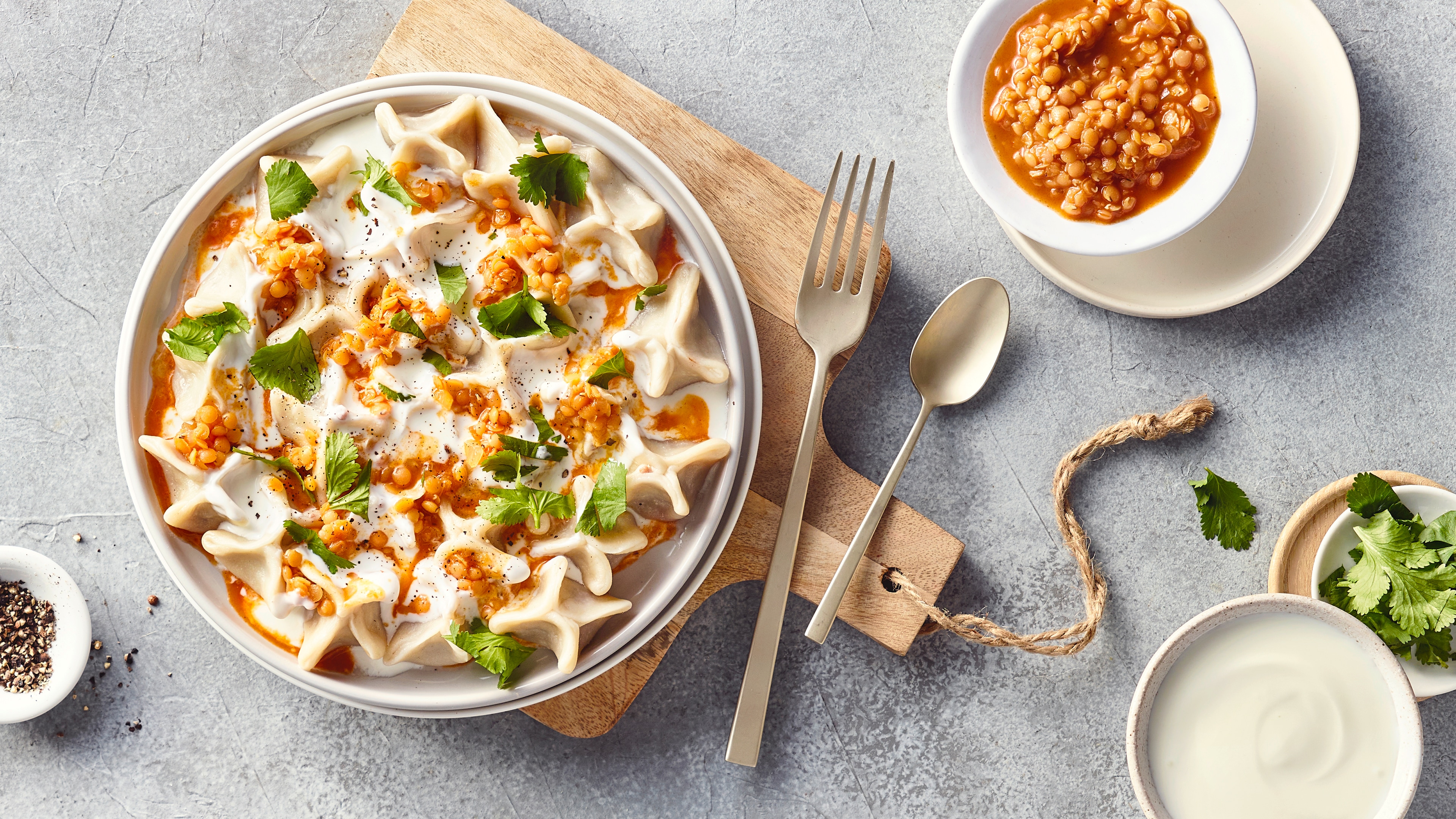 Ein Teller mit gefüllten Teigtaschen, bedeckt mit weißer Sauce, garniert mit gehackten Kräutern und kleinen Körnern