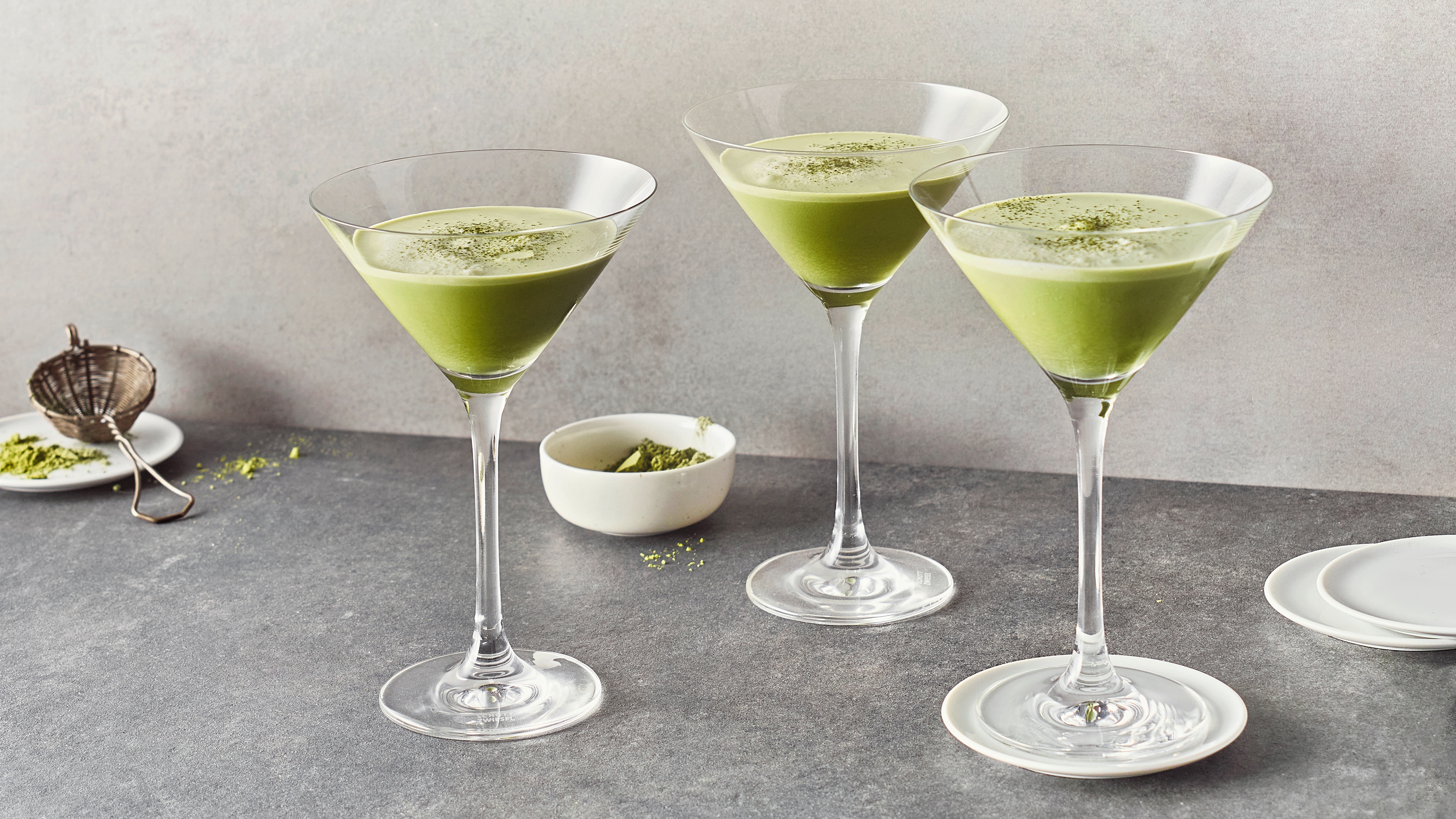 Cocktail-Rezept für Matcha Martini Martini-Gläser, befüllt mit einem hellgrünen Getränk mit einen kleinen hellgrünen Schaumrand, garniert mit etwas grünem Pulver