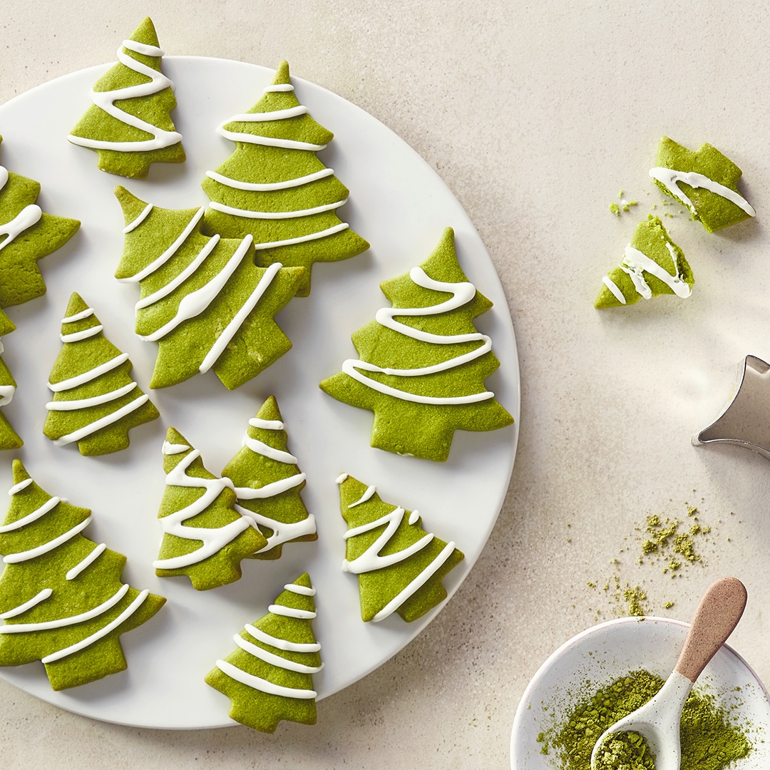 Ein Teller mit grünen Tannenbaumkeksen aus Teig, verziert mit weißen Zuckergussstreifen