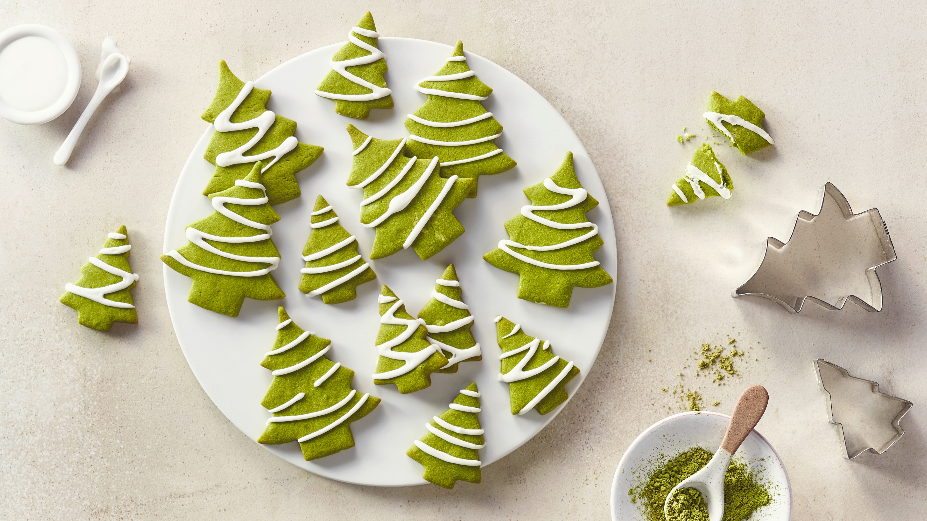 Ein Teller mit grünen Tannenbaumkeksen aus Teig, verziert mit weißen Zuckergussstreifen